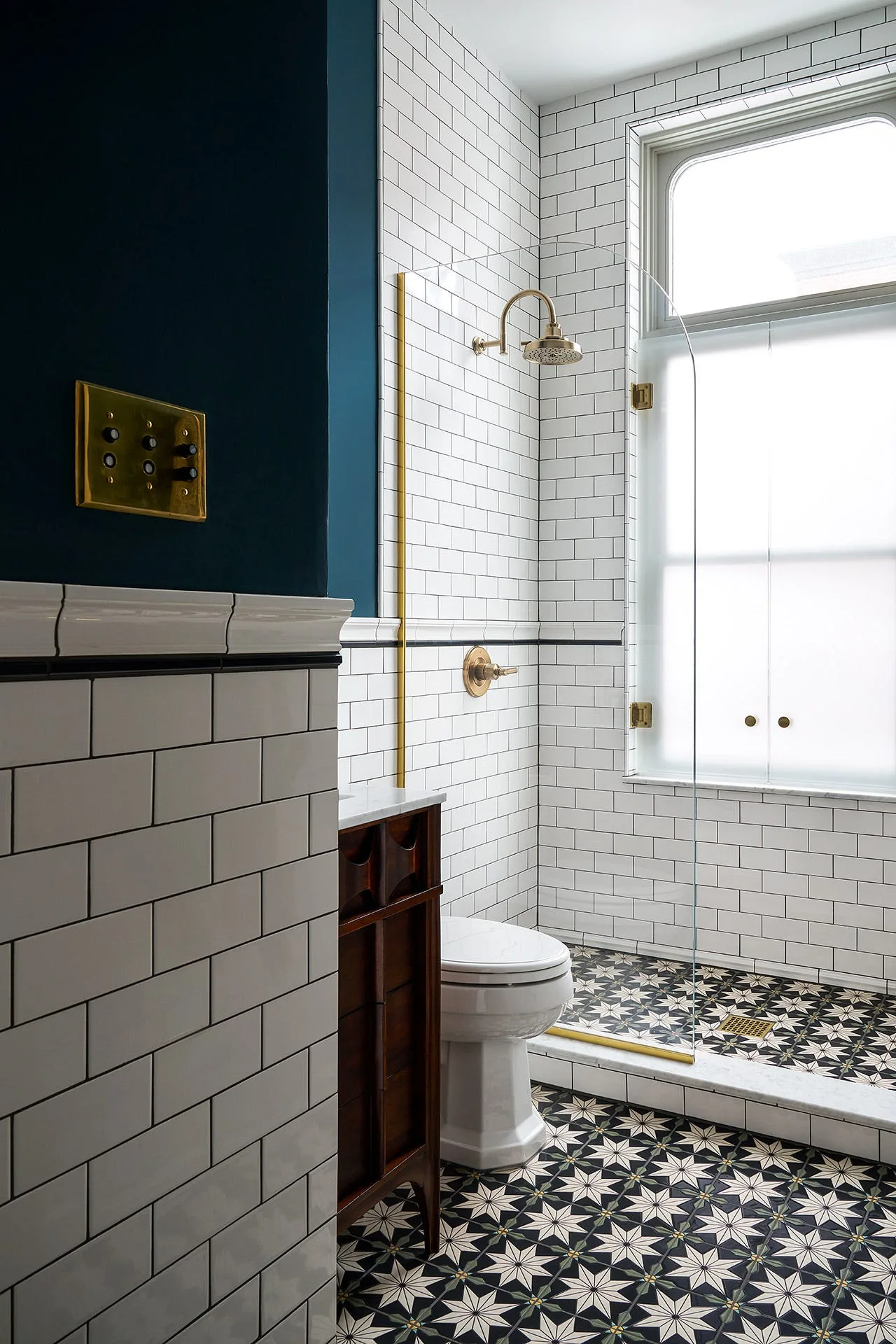 A modern bathroom features white subway tiled walls, a dark wood vanity, geometric star floor tiles, and contrasting brass fixtures.