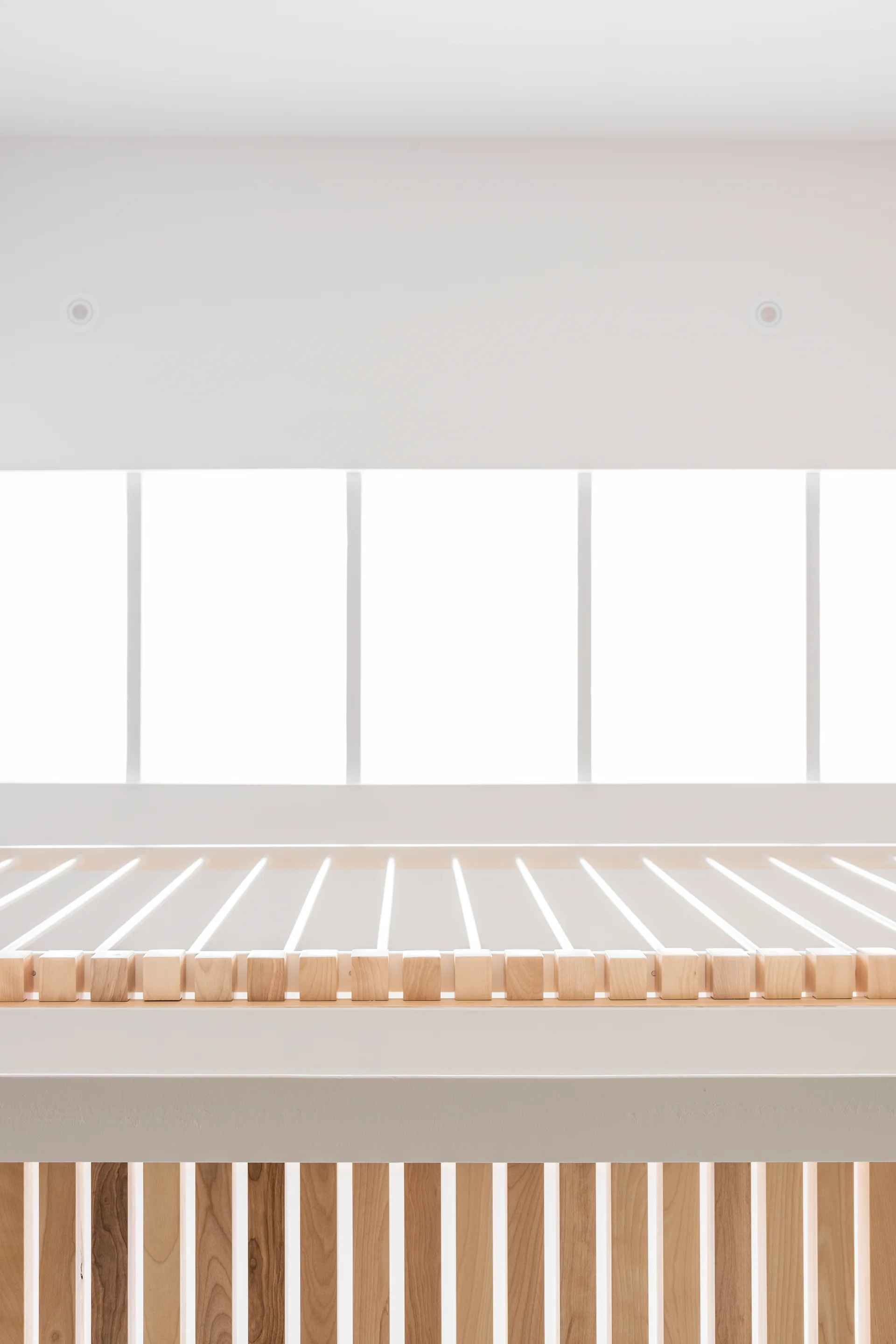 Vertical light wood slats form a geometric privacy screen set against bright white walls and recessed ceiling lights in a minimalist interior.