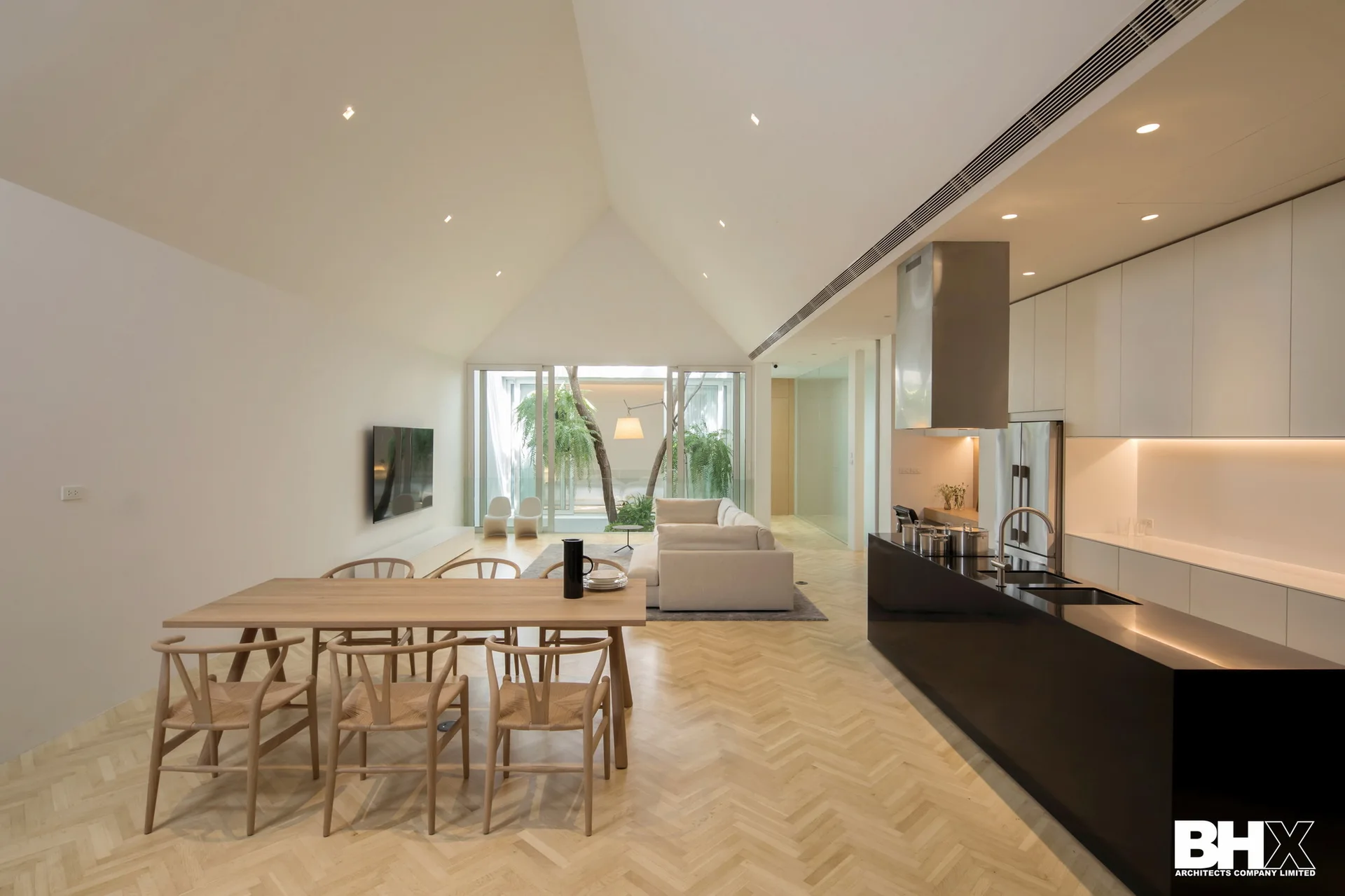A spacious open-plan interior featuring a vaulted ceiling, herringbone wood floors, a light wood dining table, and a sleek black kitchen island.