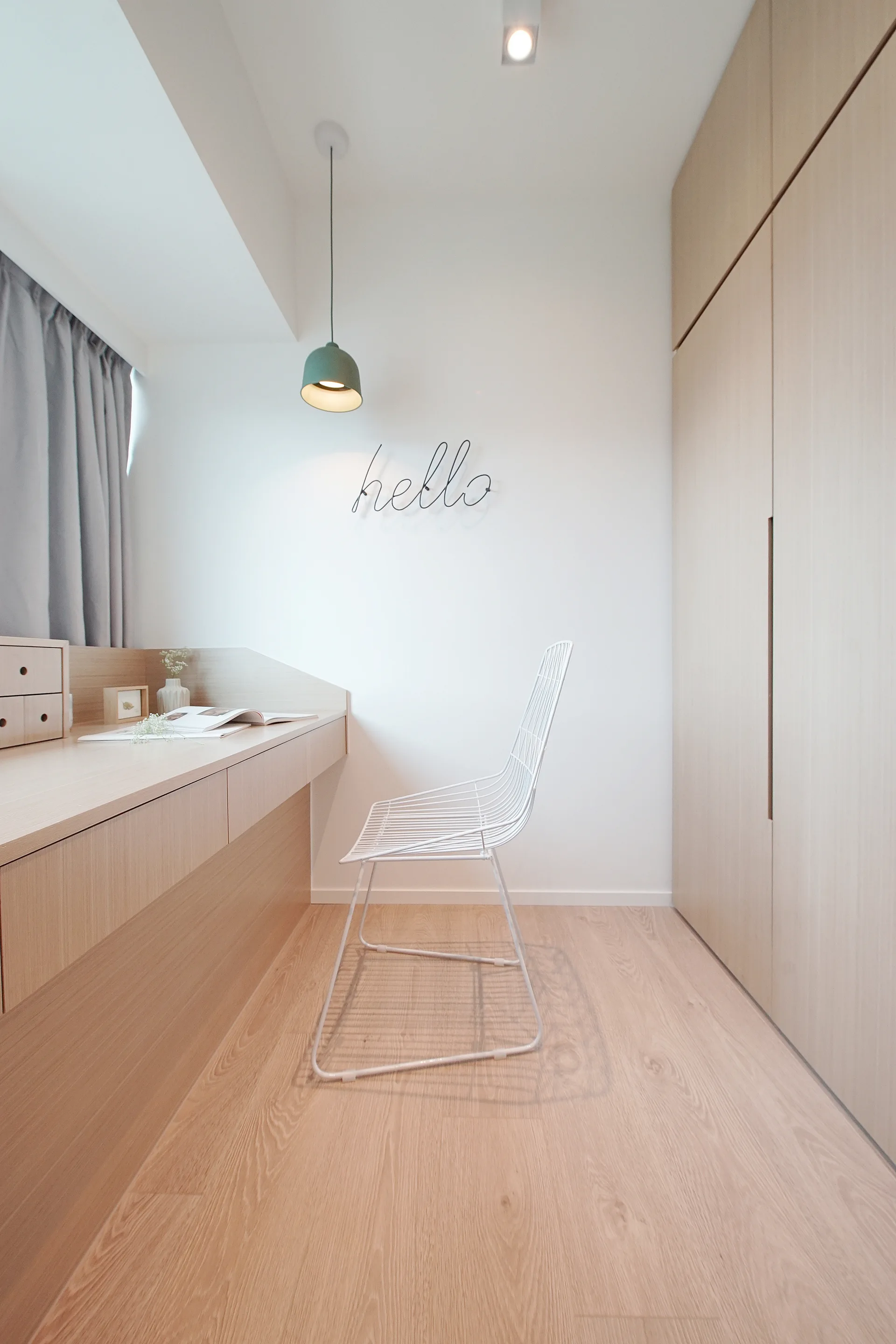 A minimalist home office featuring a light wood built-in desk, a white wire chair, and matching tall wooden wardrobes against white walls.