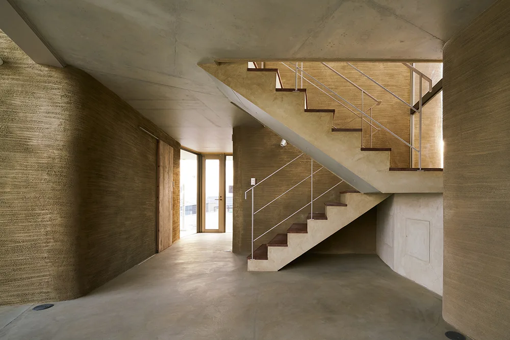 A minimalist concrete entryway with a modern staircase, thin metal handrails, and textured tan plaster walls.