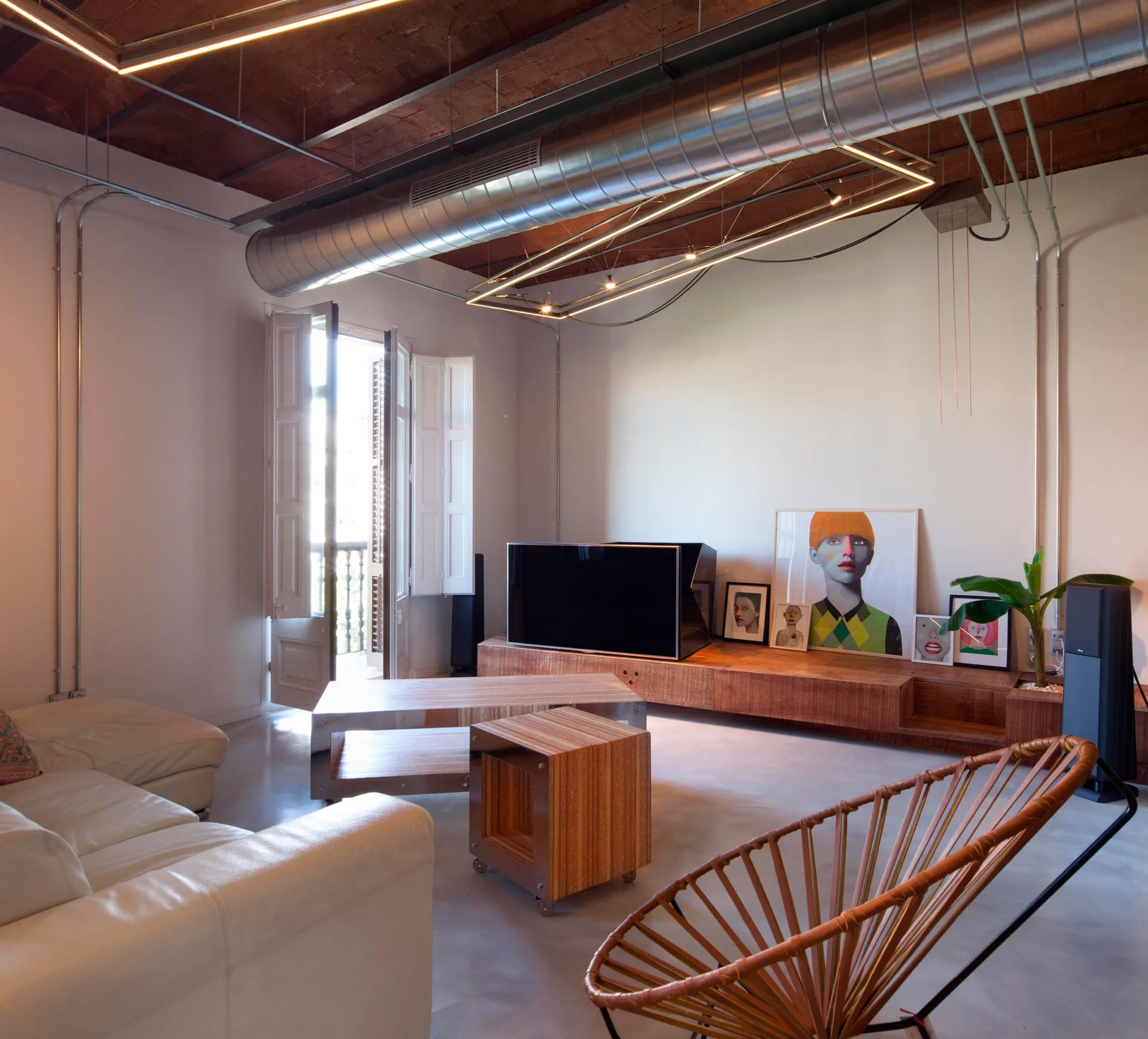 Industrial loft living room with an exposed brick ceiling, low wooden media console with framed art, and a white leather sofa.