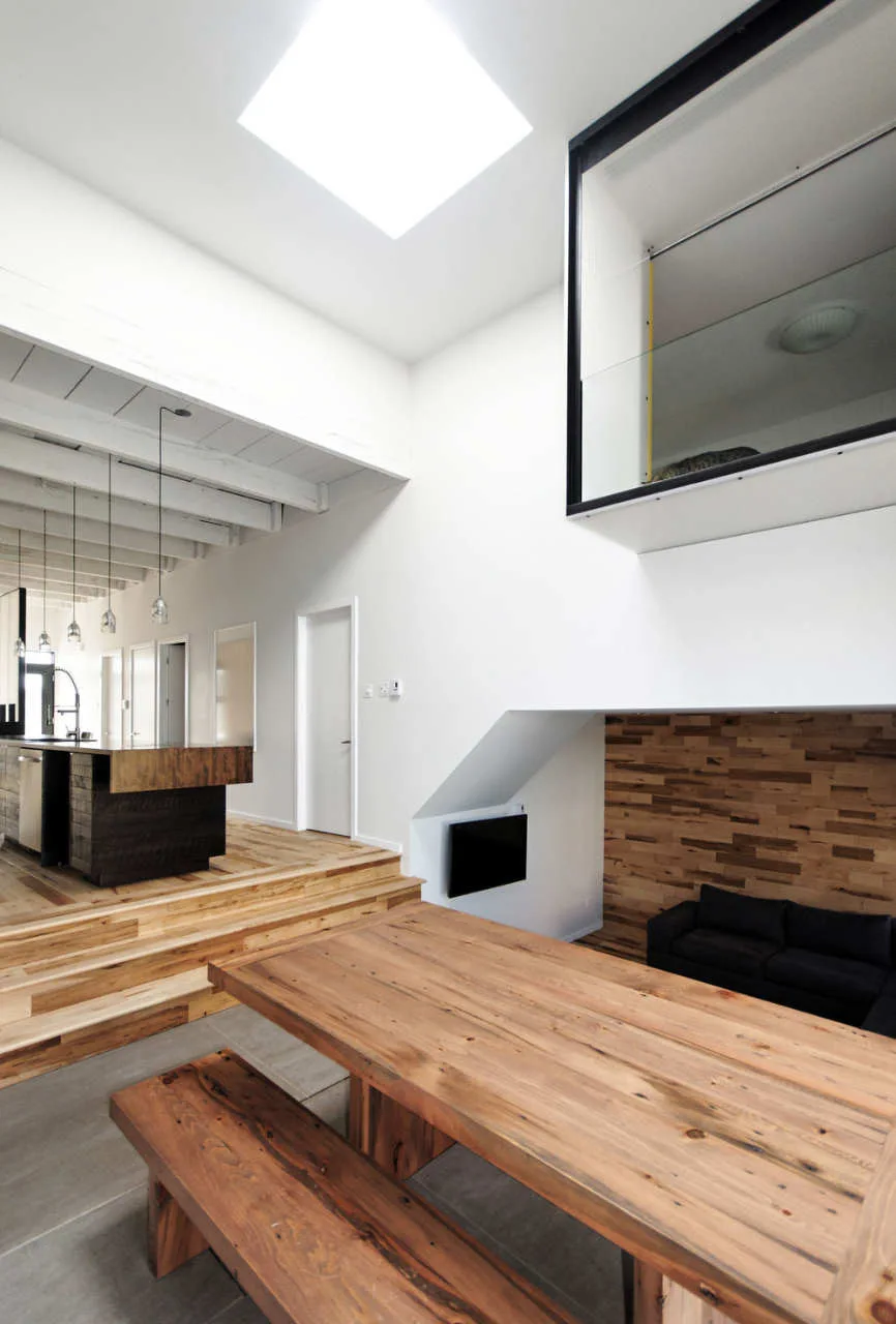 A split-level dining space features a solid wood table and bench, with steps leading up to a kitchen and a skylight overhead.