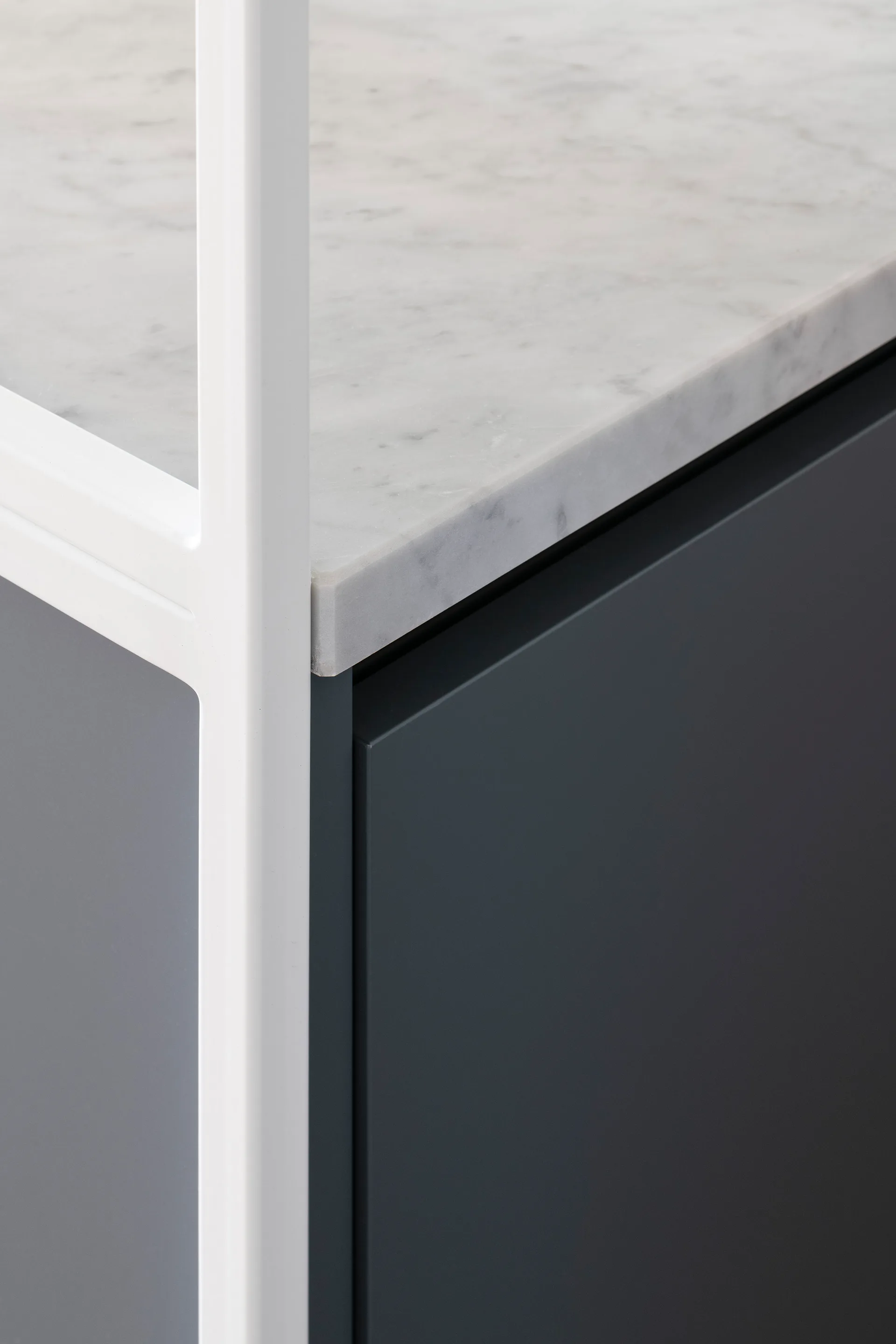 A close-up of a matte dark gray cabinet front fitted with a white veined marble countertop and a white metal support frame.