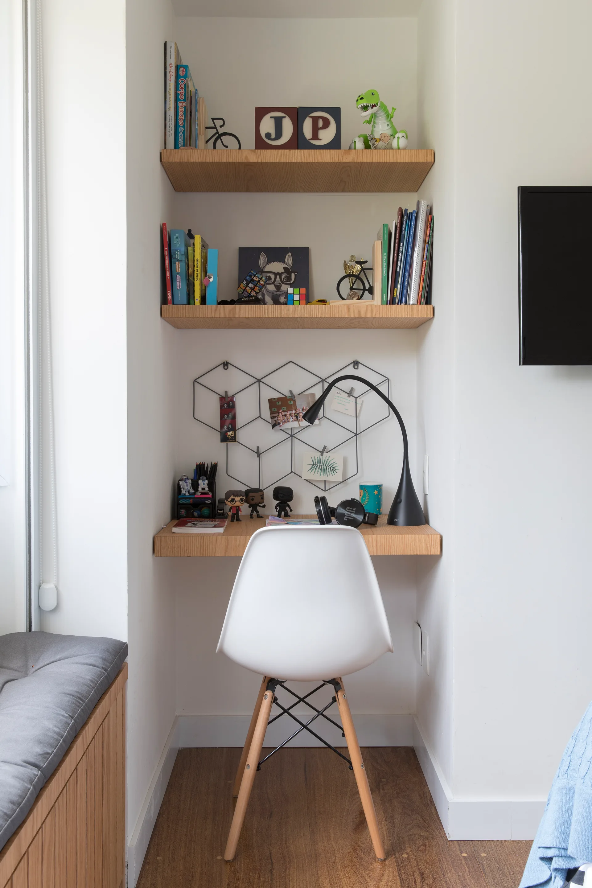 A compact white study nook featuring a built-in wooden desk, matching floating shelves, and a white molded plastic chair with wooden legs.