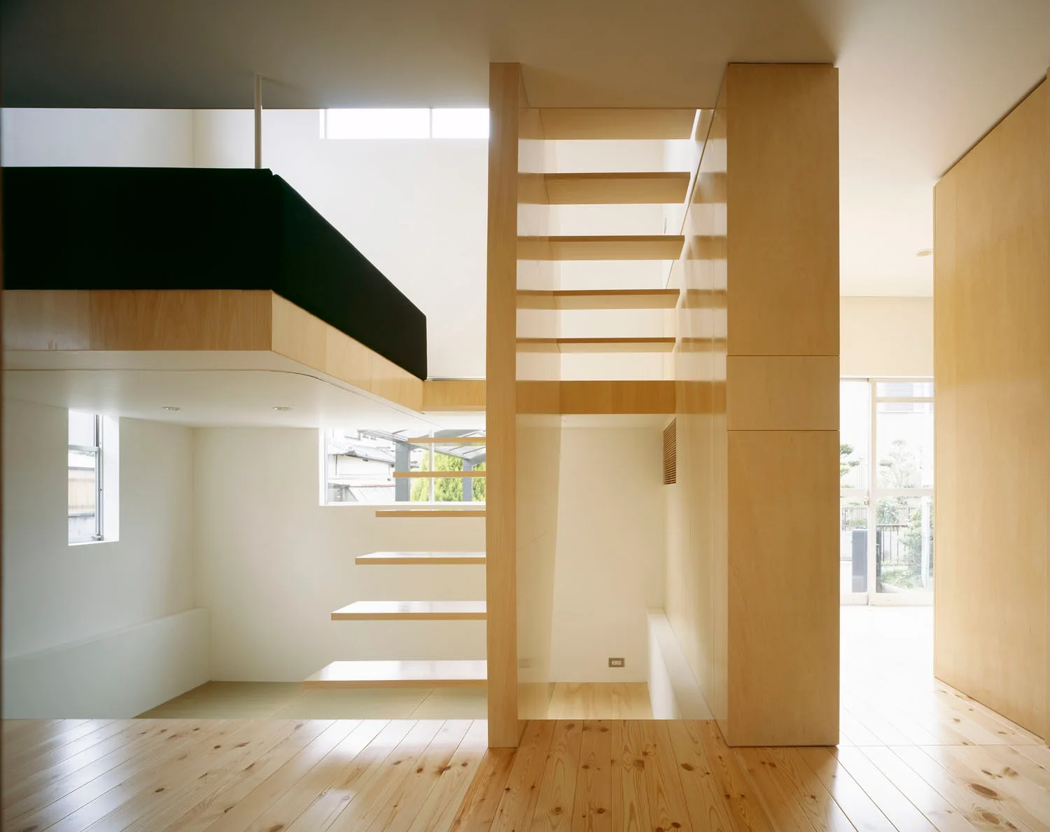 A modern loft interior features a floating wooden staircase connecting multiple levels with white walls and natural pine floors.