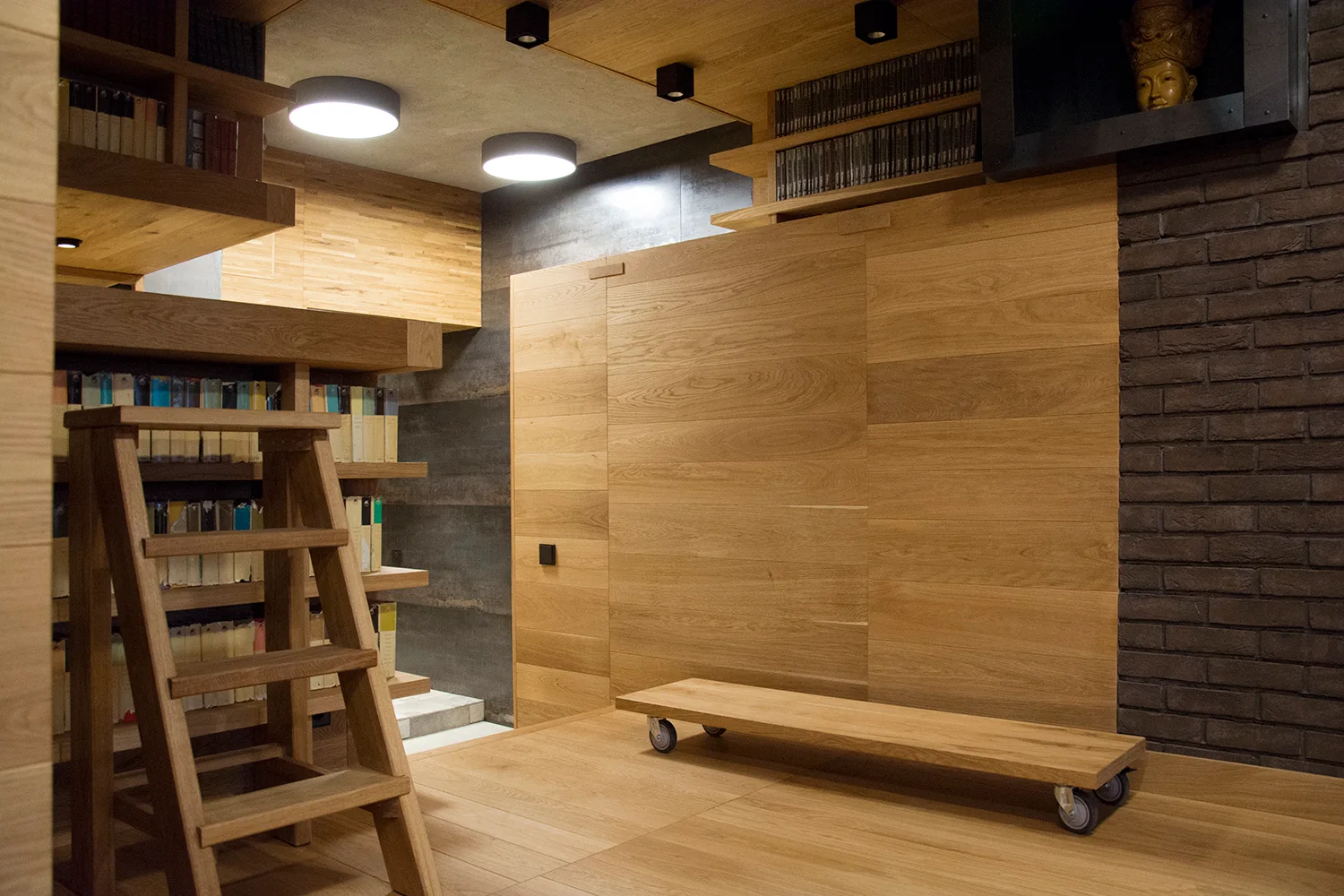 A modern home library featuring wood-paneled walls and ceiling, built-in bookshelves filled with books, a wooden step ladder, and a dark brick accent.