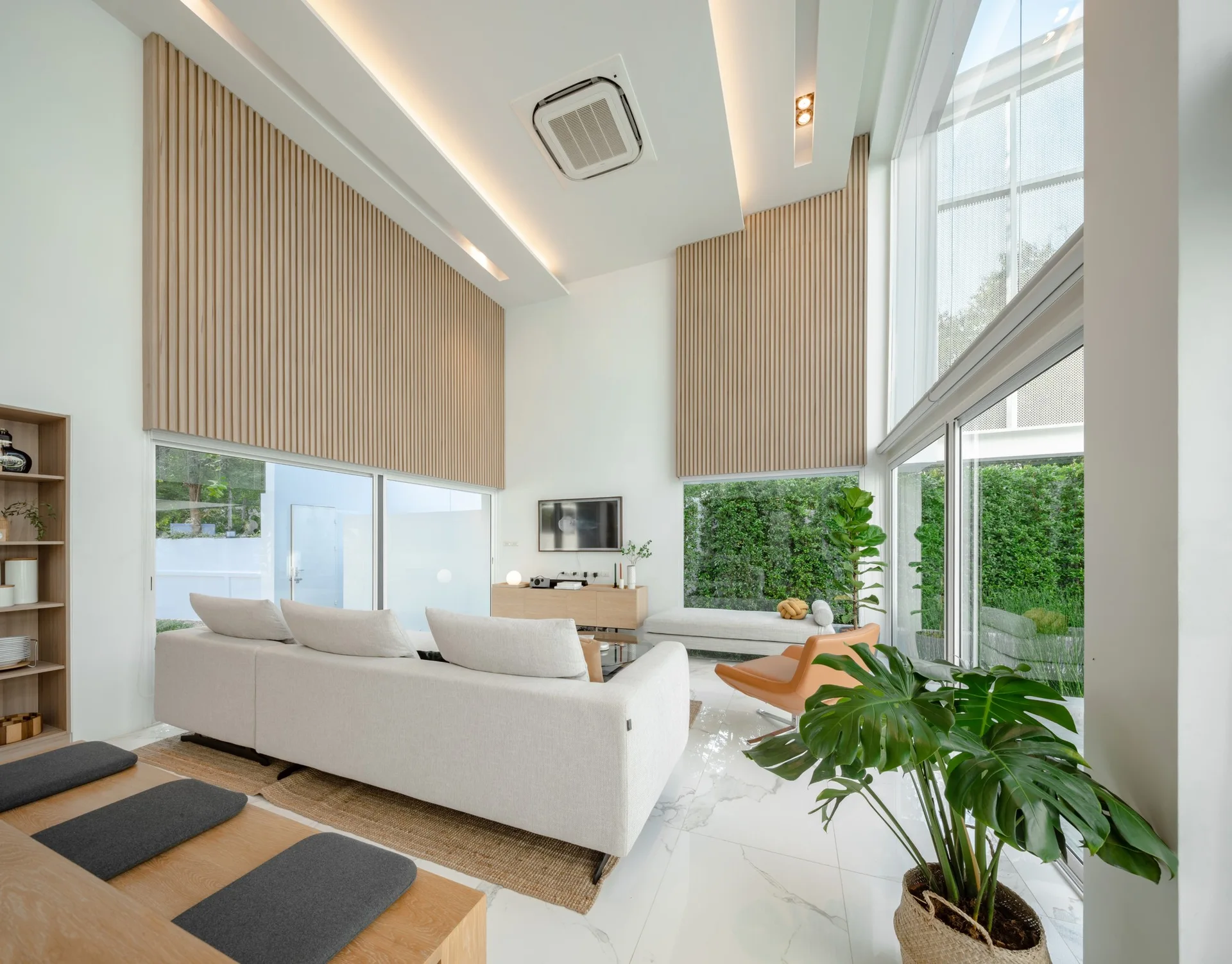 A bright living room featuring a cream sectional sofa, polished marble floors, and vertical wood slat paneling on a high accent wall.