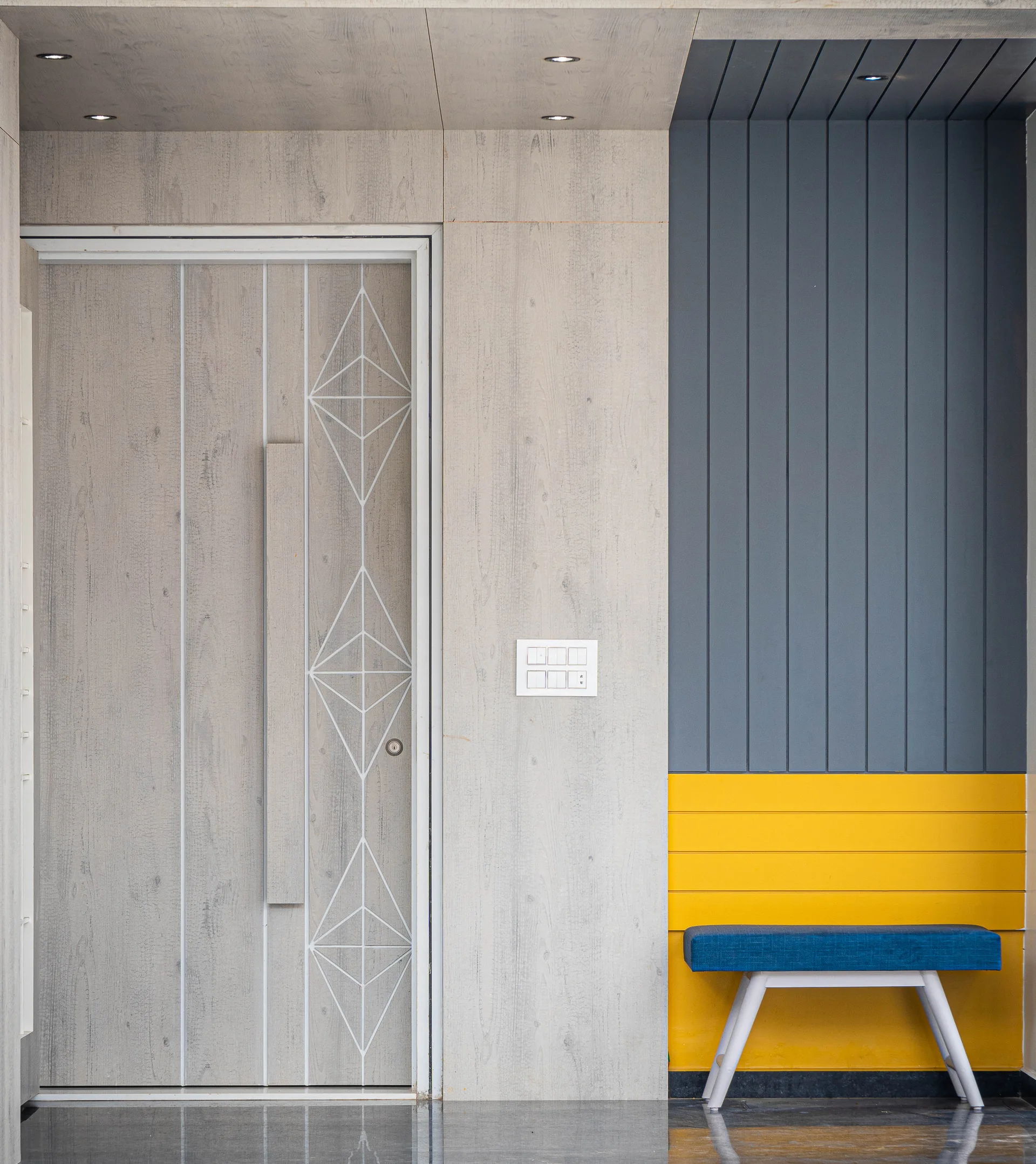 A light wood door with white geometric patterns next to a blue and yellow paneled accent wall and a small blue bench.