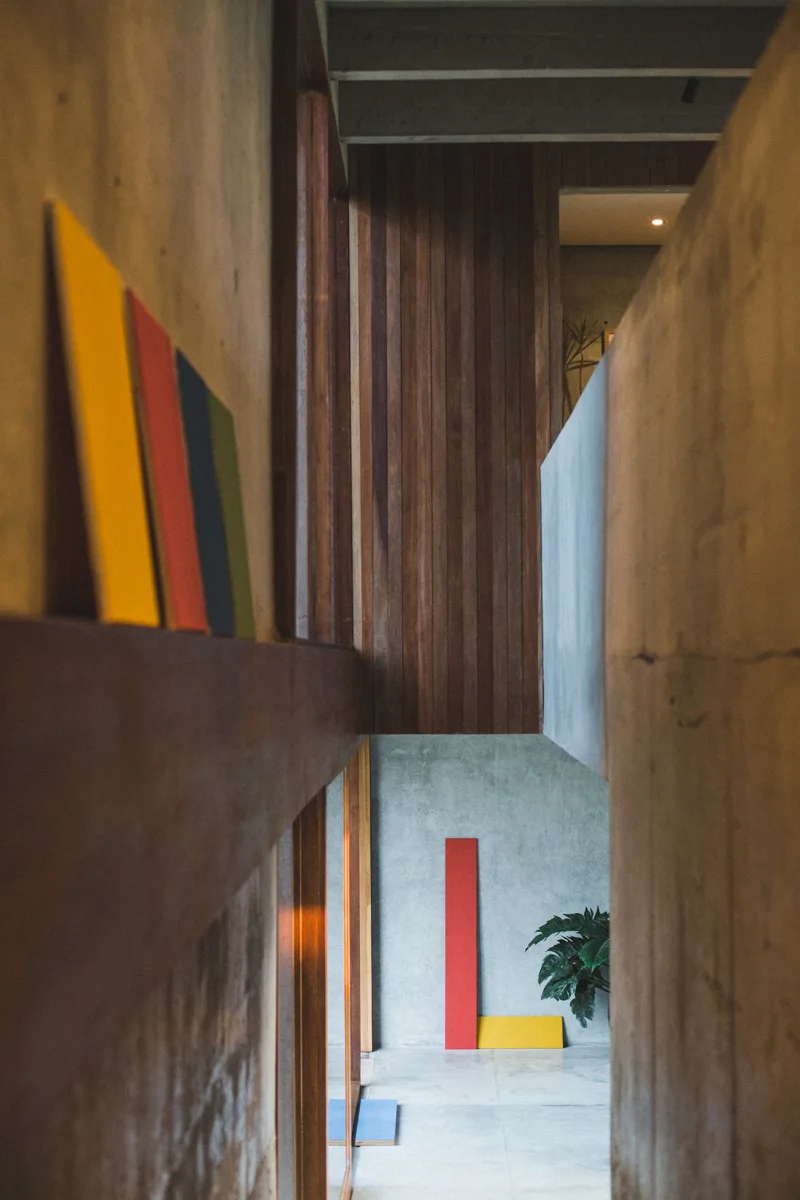 A modern architectural interior features raw concrete walls, vertical wood slat paneling, and standing rectangular art panels in red, yellow, and blue.