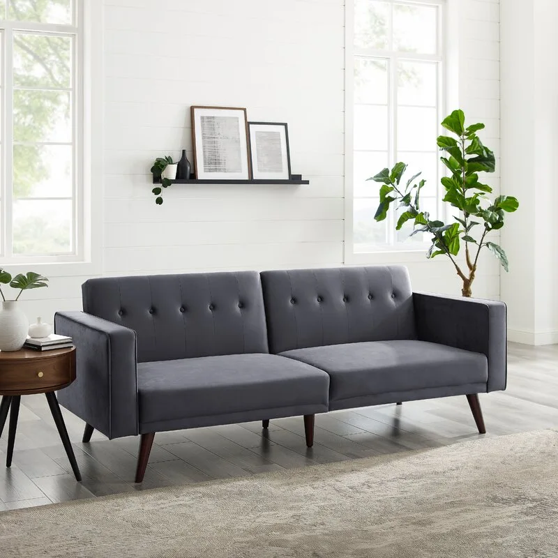 A dark grey tufted sofa with tapered wooden legs sits in a bright living room with white shiplap walls and two large windows.