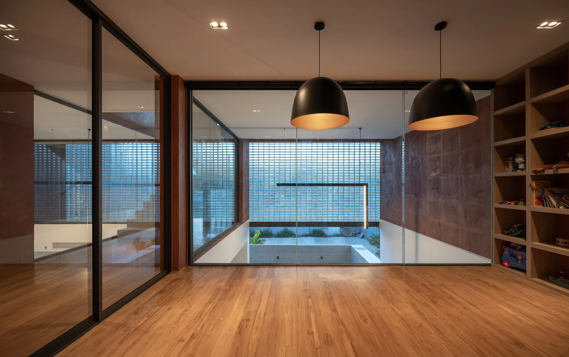 A modern interior room features warm wood flooring, large floor-to-ceiling glass partition walls, and two hanging black dome pendant lights.
