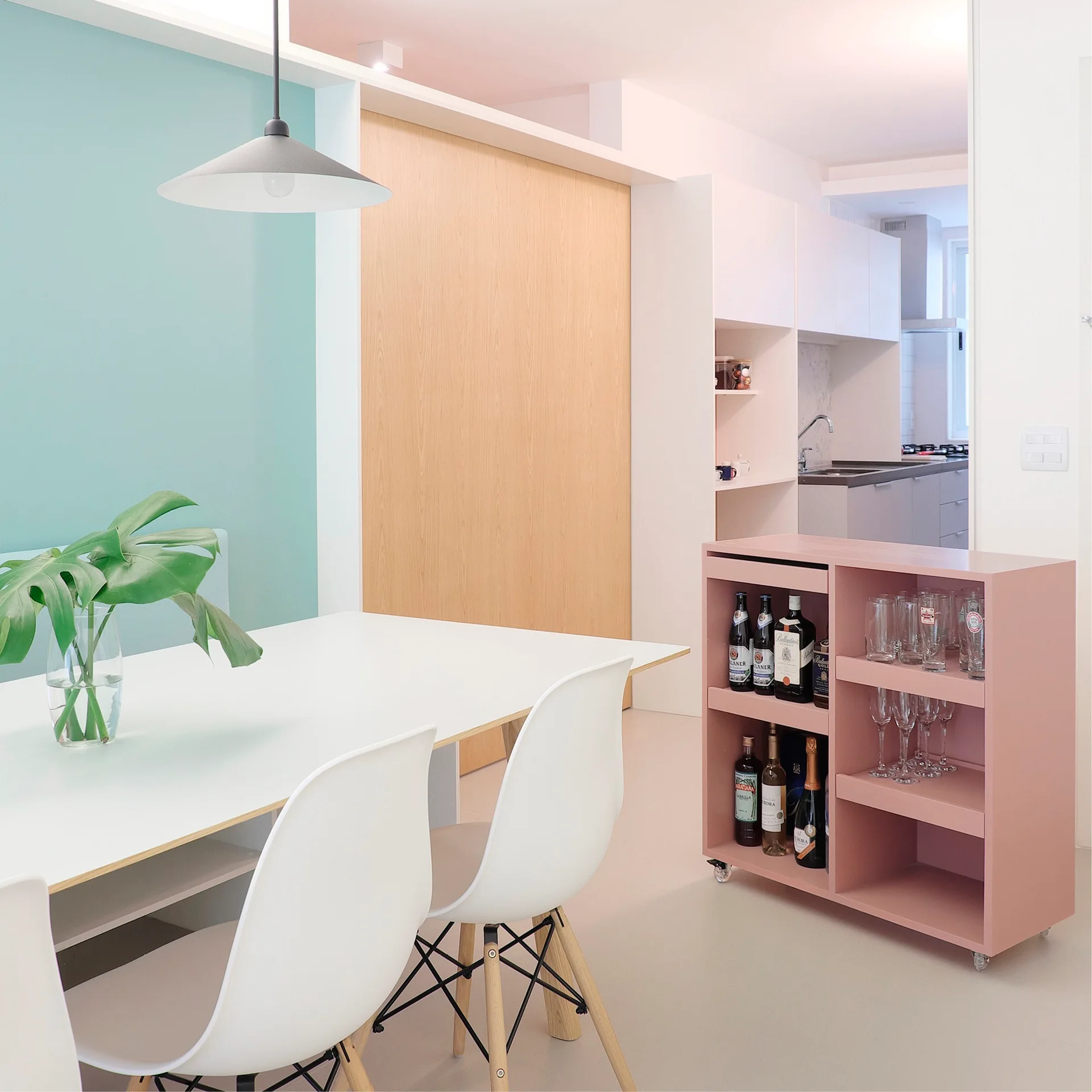 A modern dining room features a white table and chairs next to a mint green accent wall, a light wood sliding door, and a pink rolling bar cart.