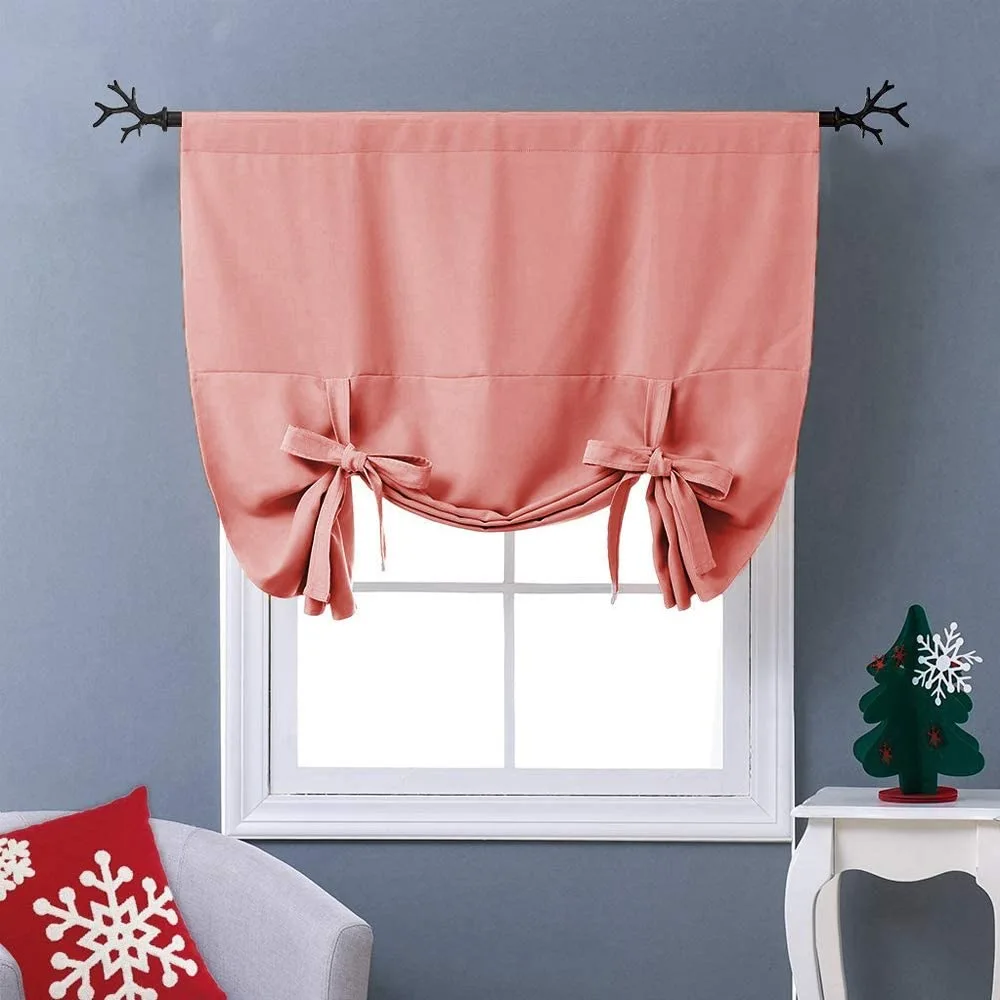A dusty pink fabric tie-up window shade hangs from a black metal curtain rod with branch-shaped finials over a white frame.