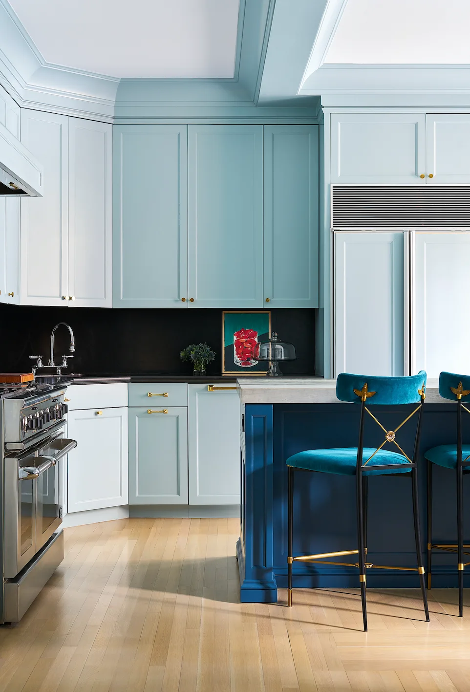 A light blue kitchen featuring a contrasting deep blue island with blue velvet barstools, a black backsplash, and light wood flooring.