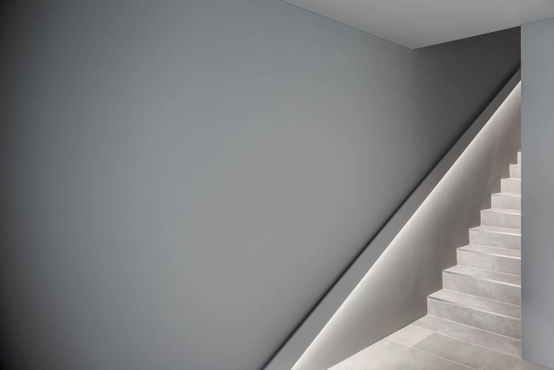 A minimalist grey staircase features stone-like steps and a recessed linear LED light strip glowing beneath the handrail.