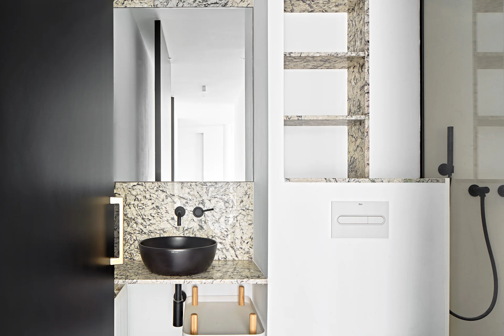 A modern bathroom vanity features a black vessel sink on a veined stone countertop next to matching recessed shelves.