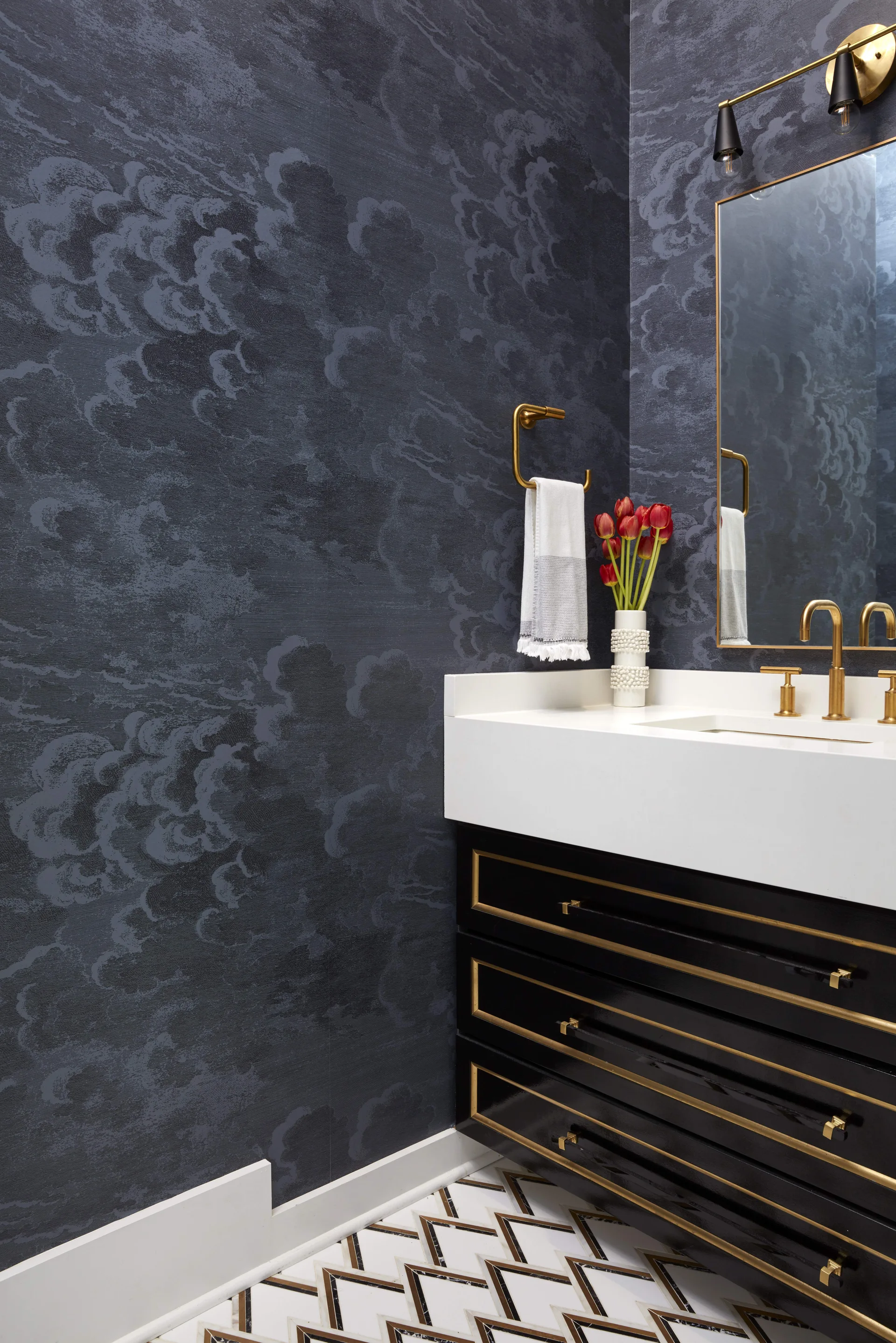 A powder room features navy cloud-patterned wallpaper, a glossy black vanity with gold trim, and geometric tile flooring.