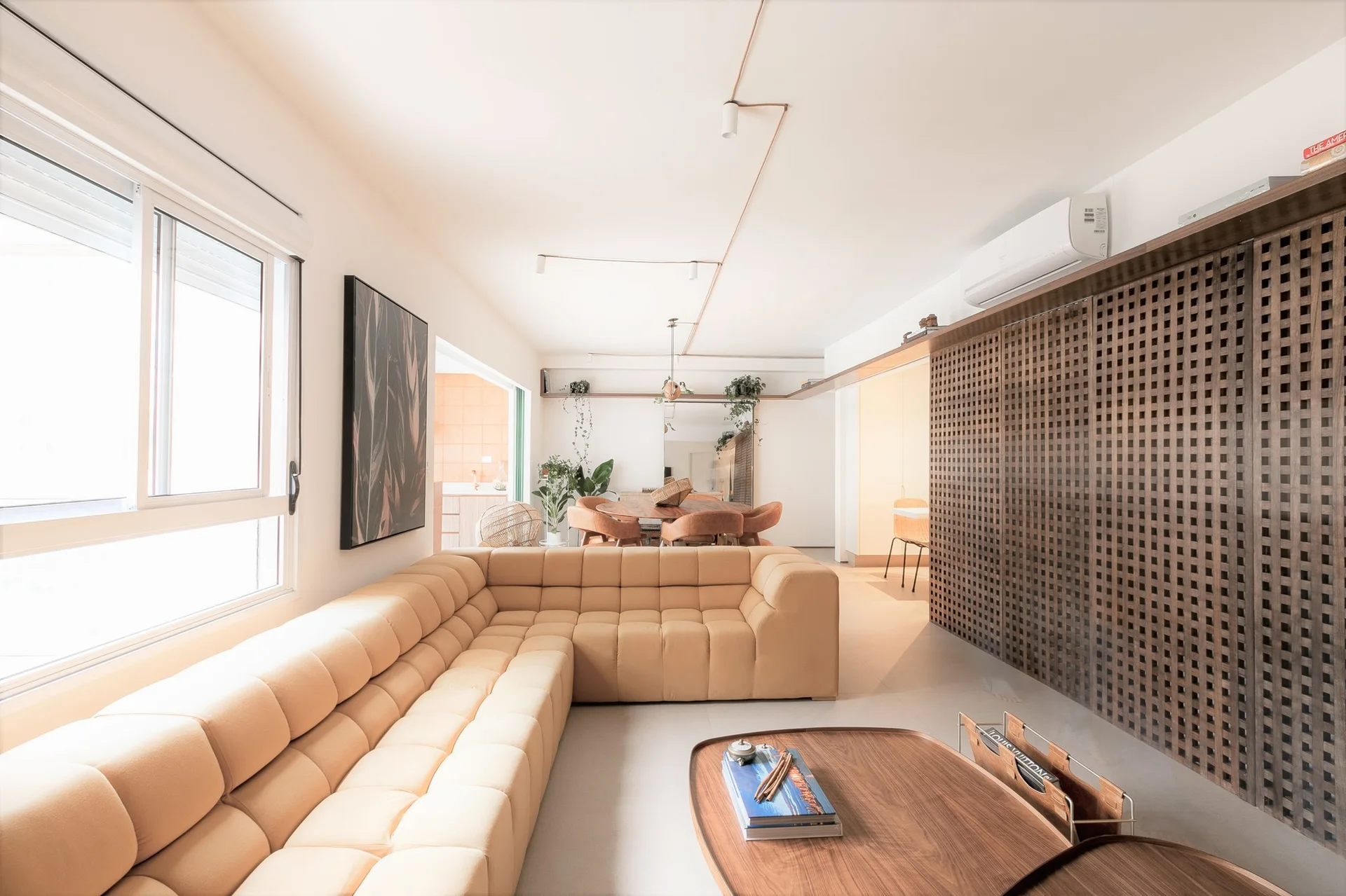 A bright open-plan living room featuring a large tan tufted modular sectional sofa and a built-in wall cabinet with dark wooden lattice doors.