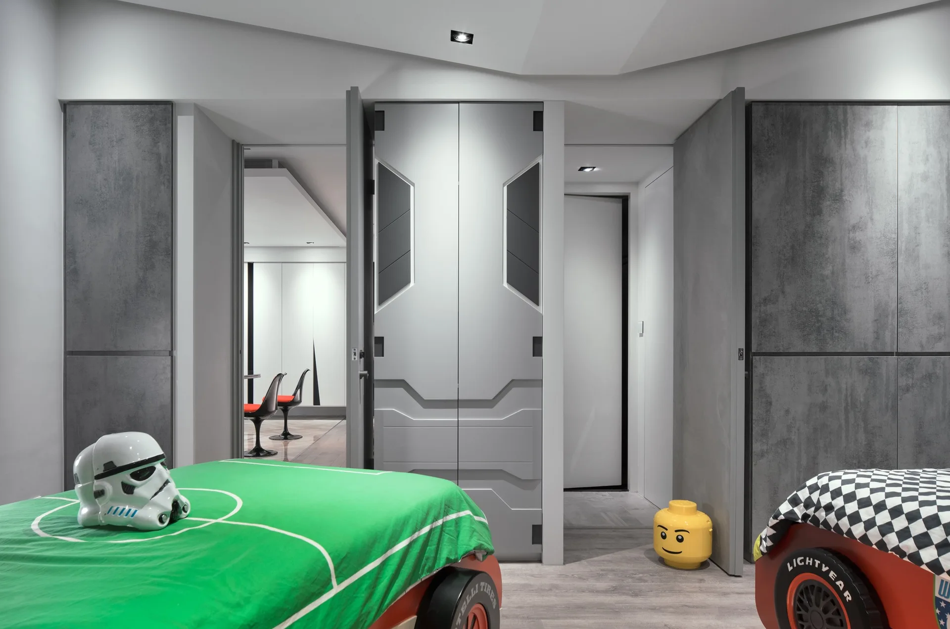 A themed kids bedroom features two red race car beds flanking a central pair of futuristic gray doors with custom geometric molding.