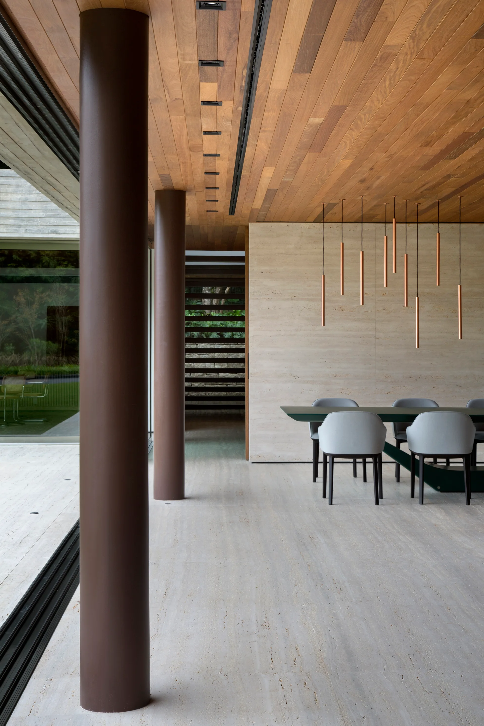 A modern dining room features a travertine floor, a wood plank ceiling, and copper cylinder pendant lights over a dark table with grey chairs.