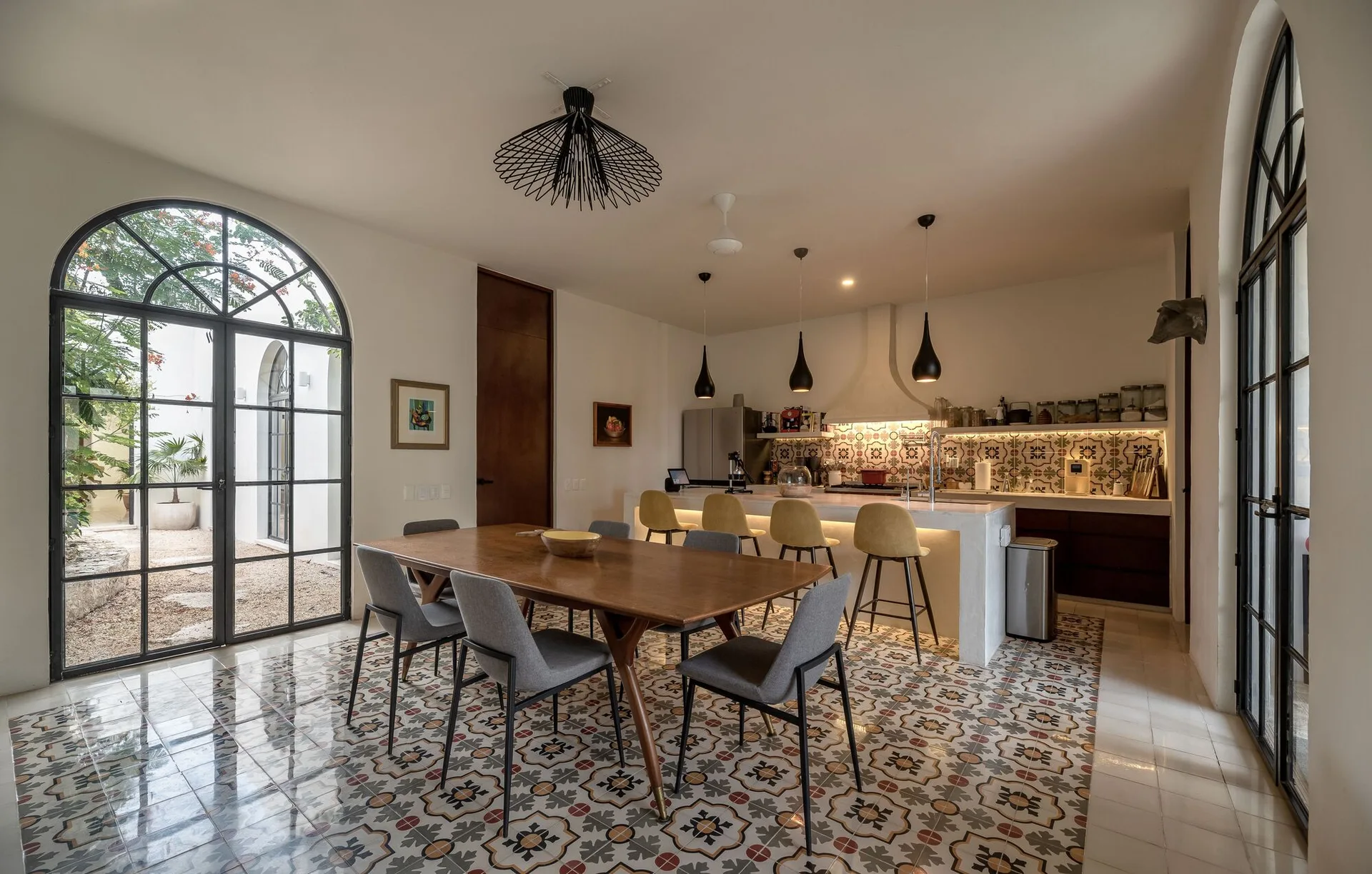 An open kitchen and dining area features a wooden table with grey chairs, a white island with yellow stools, and patterned tile flooring.