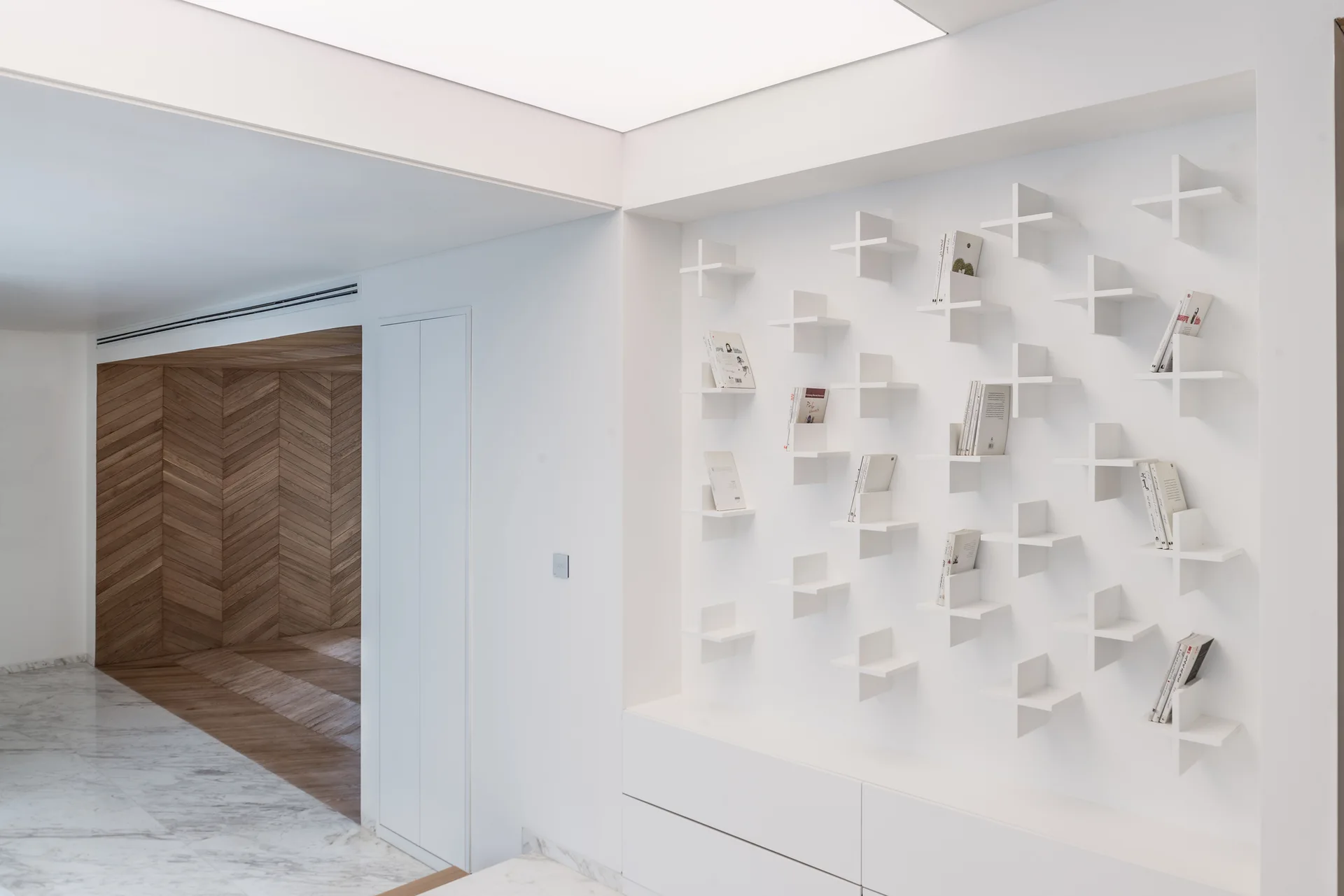 A built-in white wall shelving unit with cross-shaped dividers stands next to a doorway lined with herringbone-patterned wood paneling.