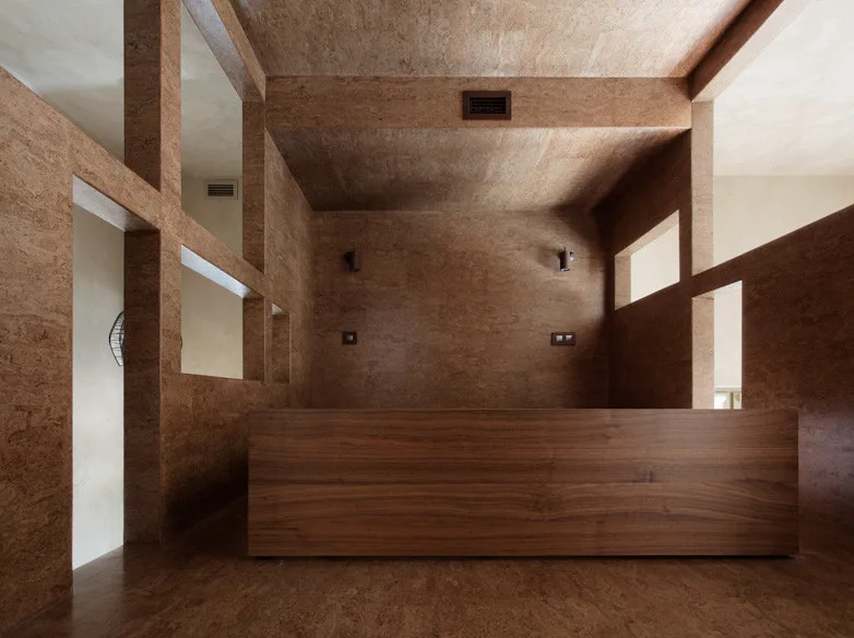 A minimalist bedroom featuring textured cork paneling on the walls and ceiling, rectangular wall cutouts, and a low wood platform bed.