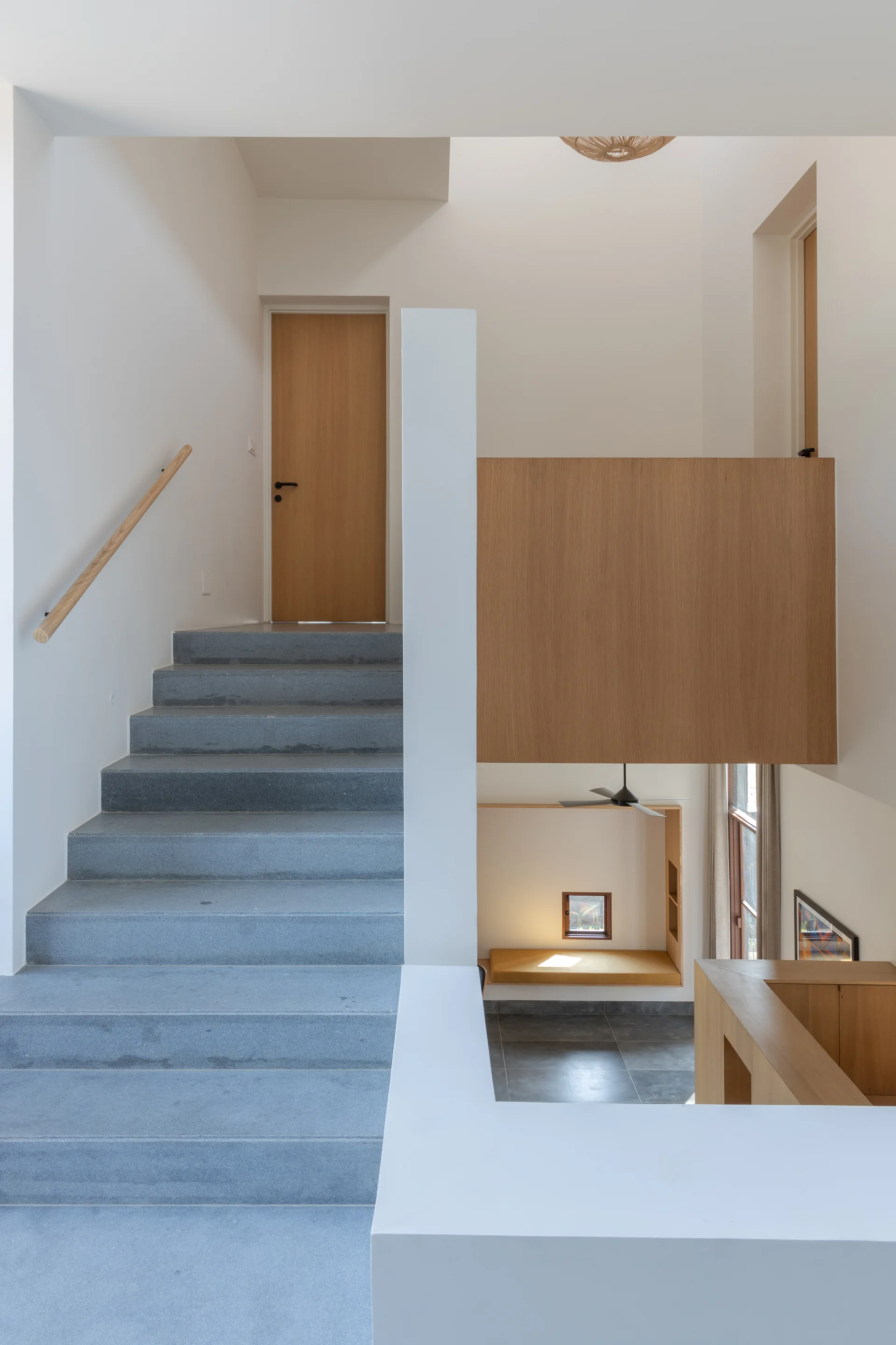 A minimalist modern staircase with gray stone steps, white walls, and a large natural wood panel element.