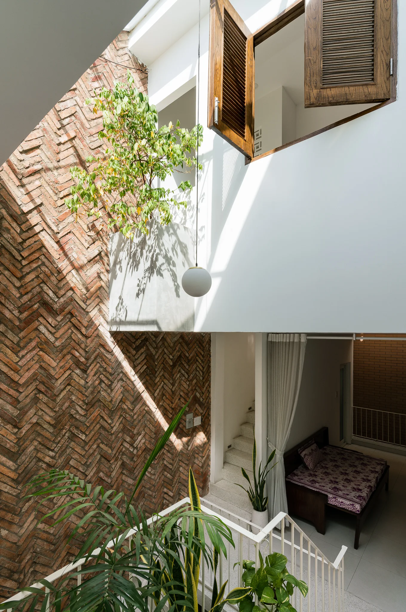 A multi-level interior courtyard features an exposed herringbone brick wall, a globe pendant light, and a window with wooden shutters.