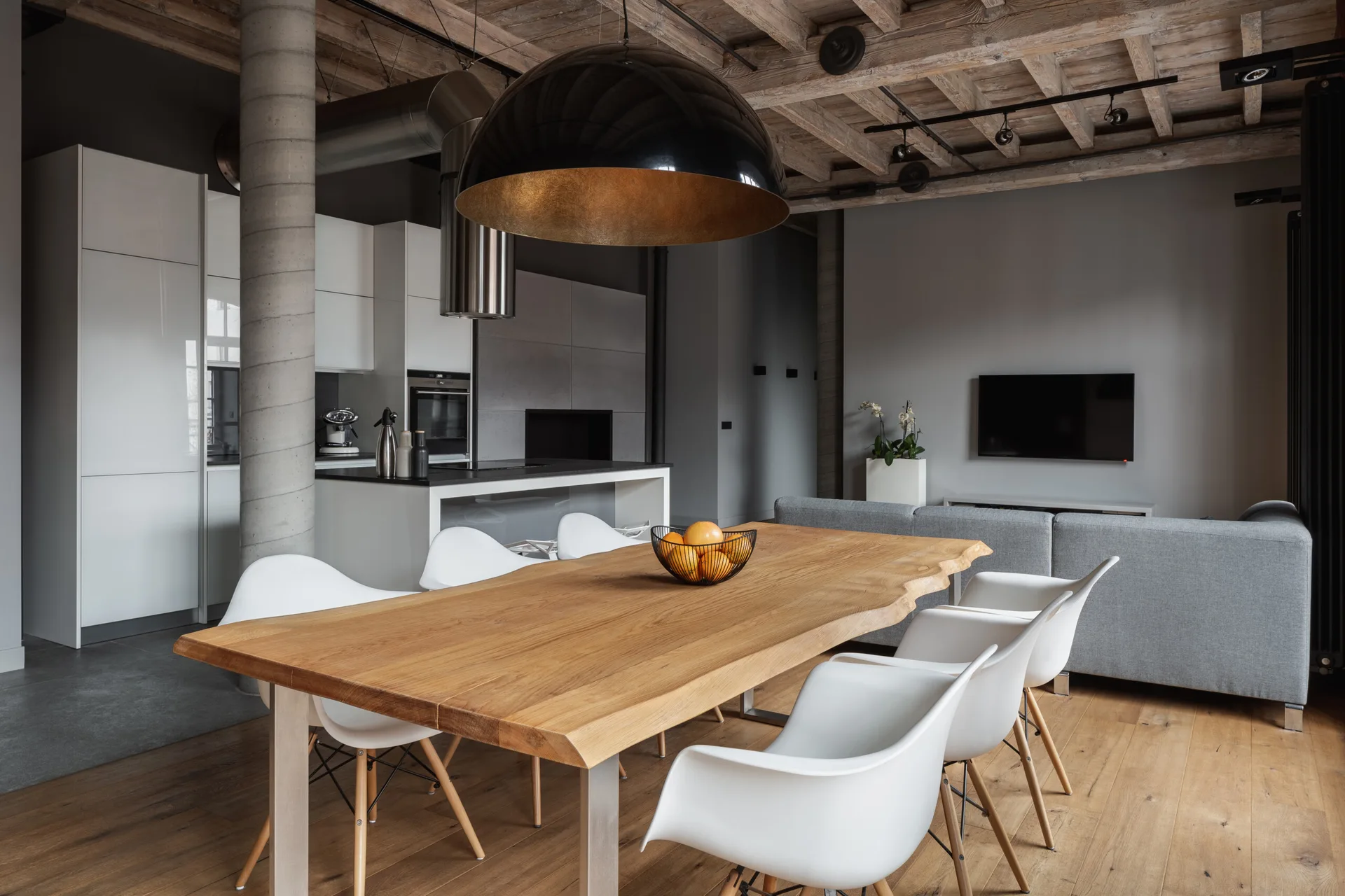 A modern open-concept dining space features a live-edge wooden table, white molded chairs, and exposed wooden ceiling beams.