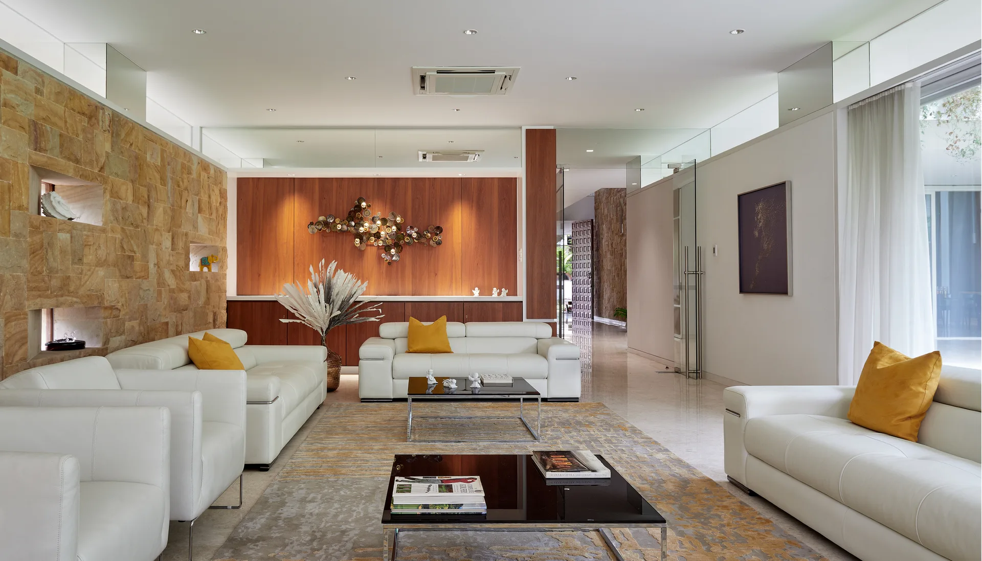 A spacious contemporary living room with white leather sofas, a textured stone accent wall, a wooden feature wall, and polished floors.
