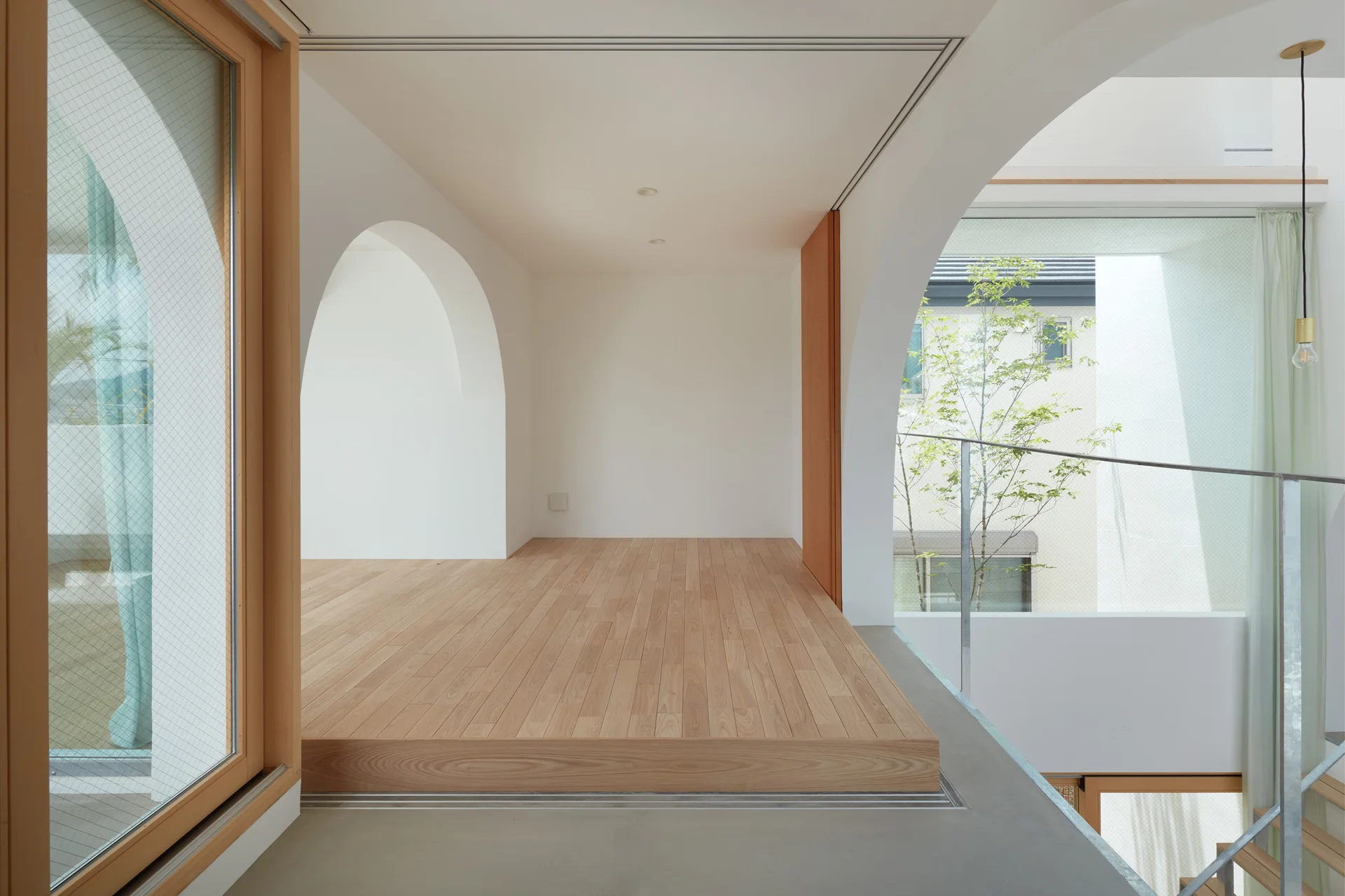 A minimalist interior landing features a raised light wood platform next to smooth white arched openings and a large glass window.
