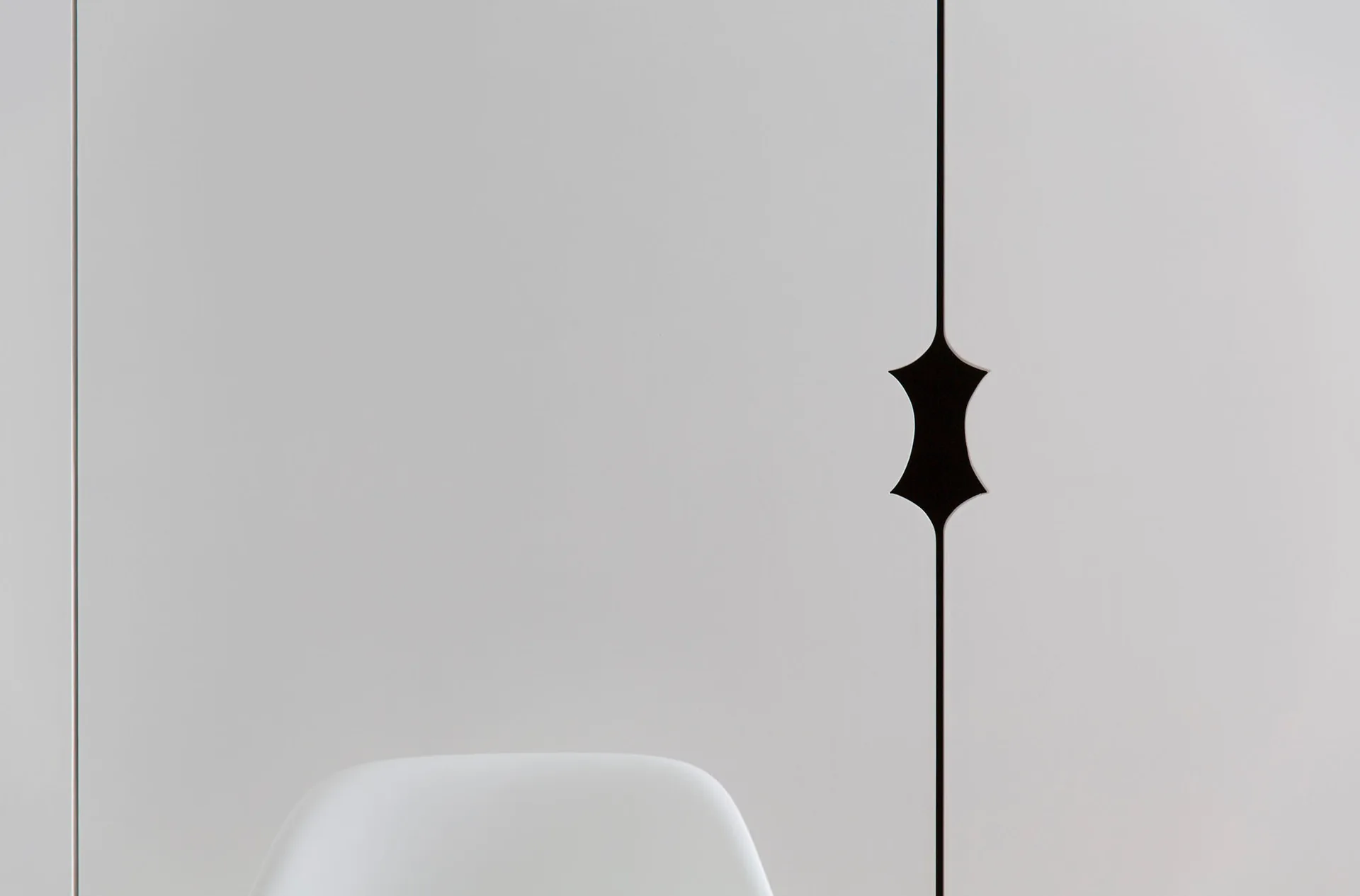Close-up of matte white cabinet doors featuring a custom recessed black geometric handle along the vertical seam above a white chair.