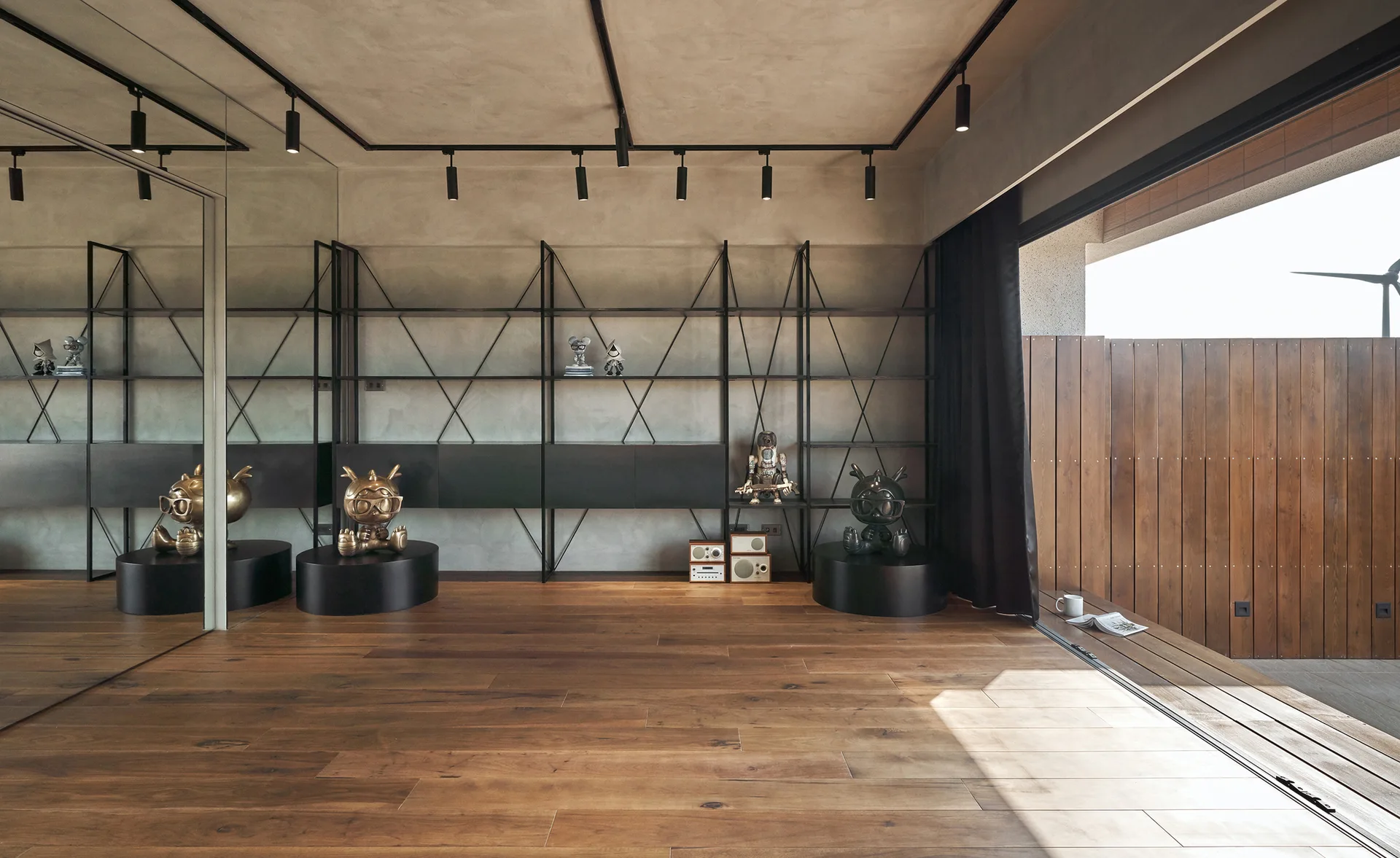 A modern room features wood plank flooring, a tall black metal shelving unit against a textured grey wall, and a full-height mirrored wall.