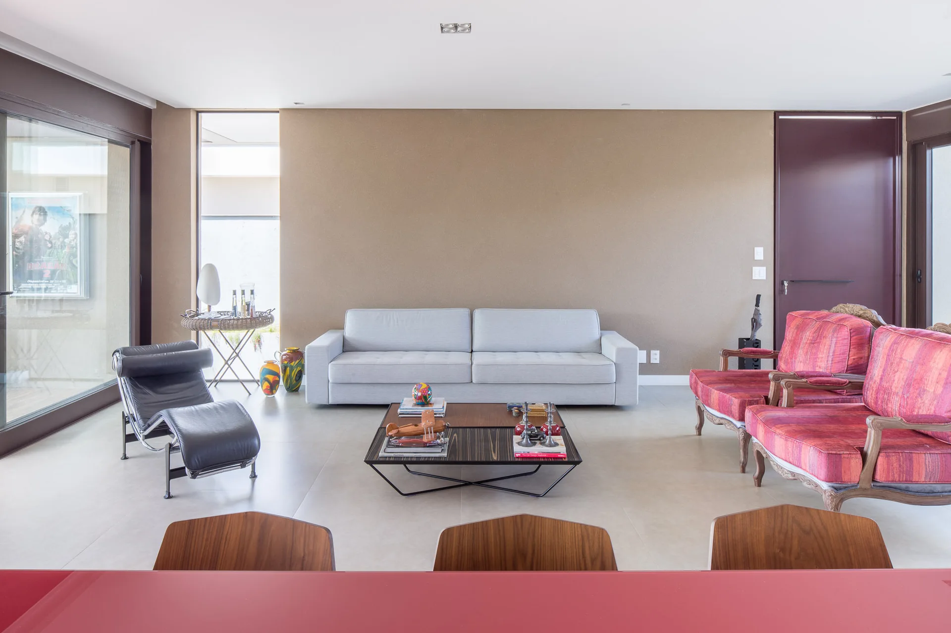 An eclectic living room features a gray sofa against a tan wall, flanked by a black leather lounge chair and two red patterned armchairs.