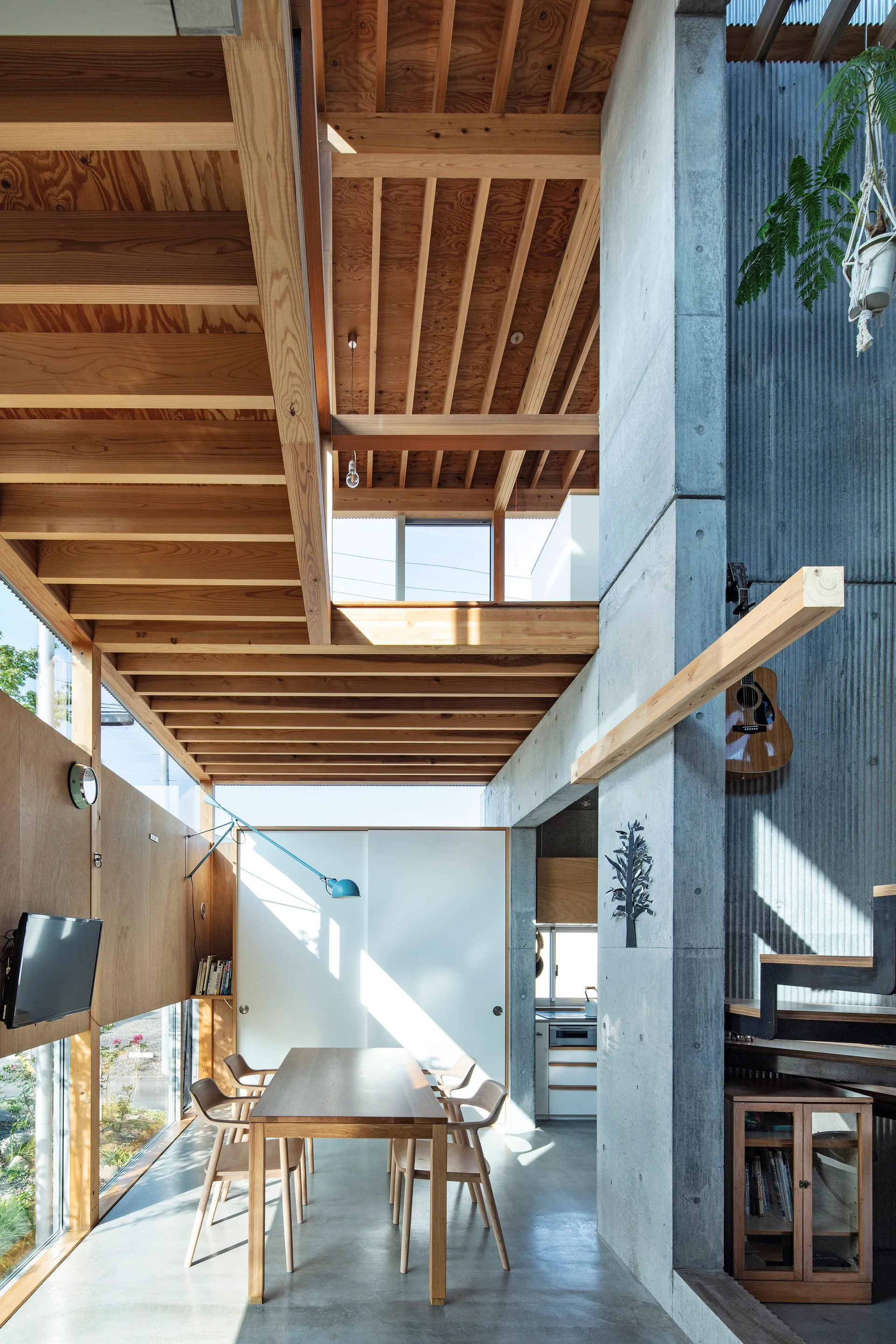 A modern dining room featuring a wooden table and chairs, set against raw concrete walls and an exposed timber joist ceiling.