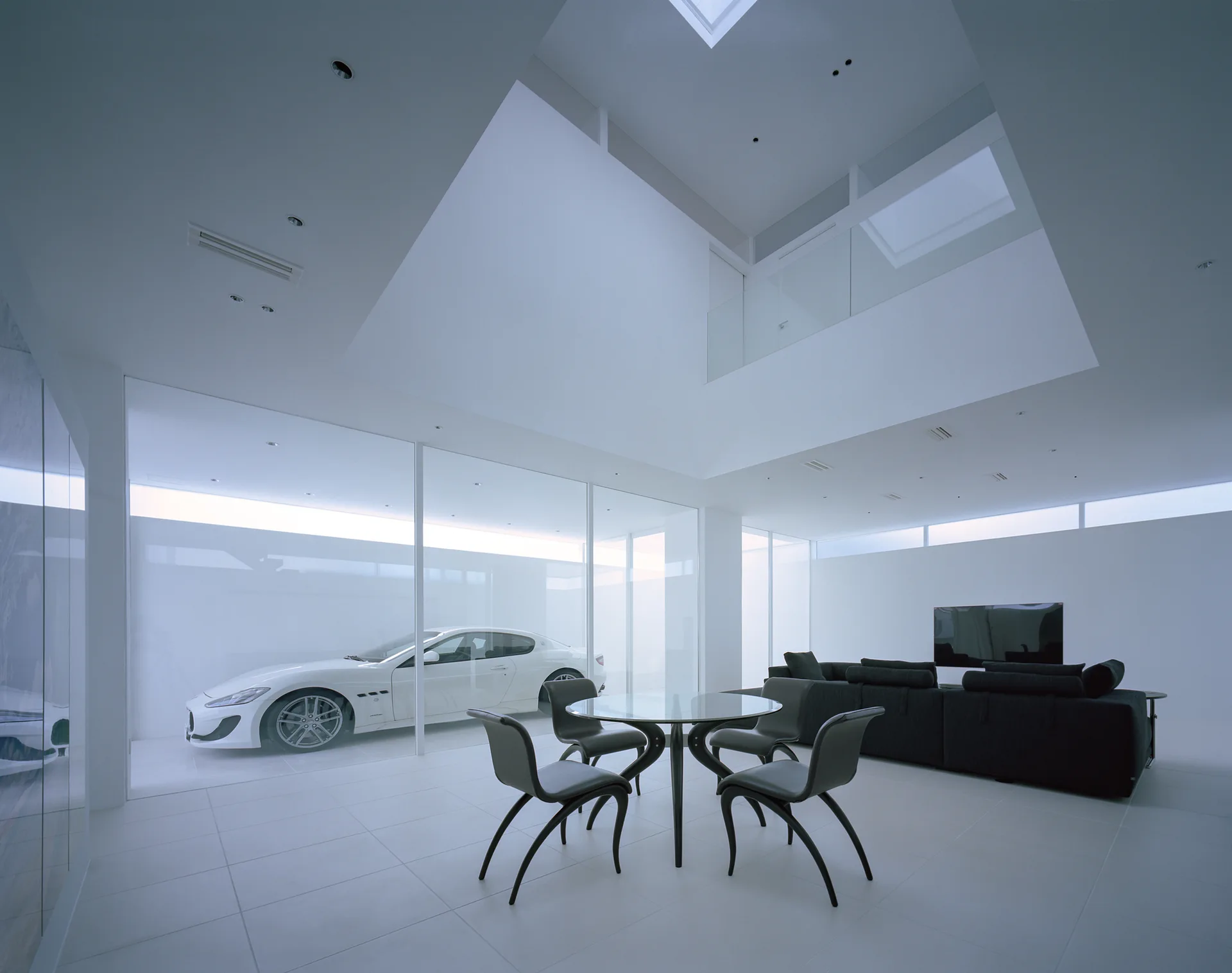 A minimalist white living area features a glass wall partition displaying a white sports car alongside a black sofa and dining table.