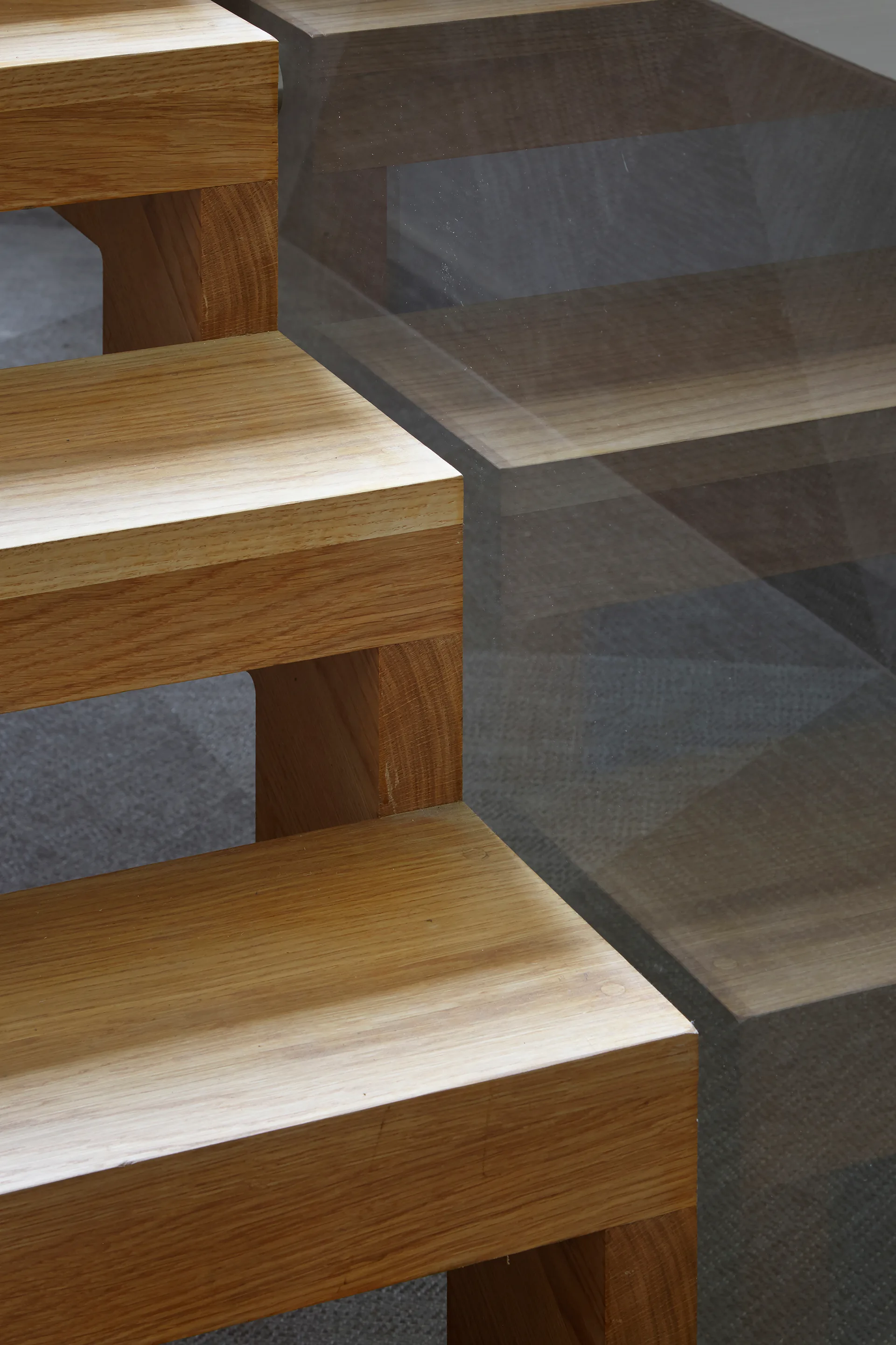 Close-up of thick wooden staircase steps with open risers next to a transparent glass panel.