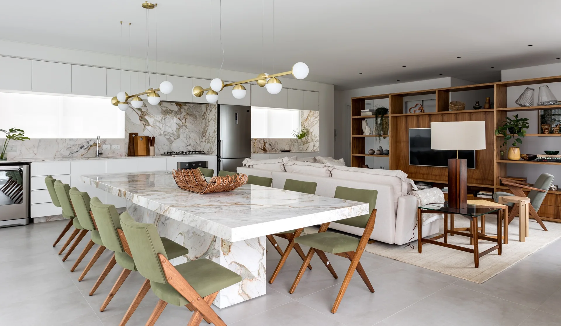 An open-plan kitchen and living area features a large veined marble island with olive green dining chairs and a modern gold globe pendant light.