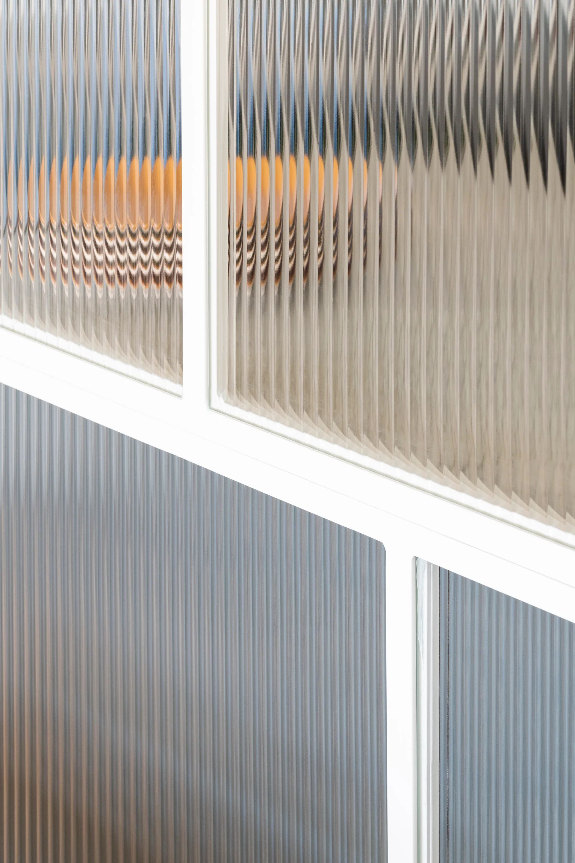 A close-up view of an interior partition wall featuring textured ribbed glass panels set within a white painted metal frame.