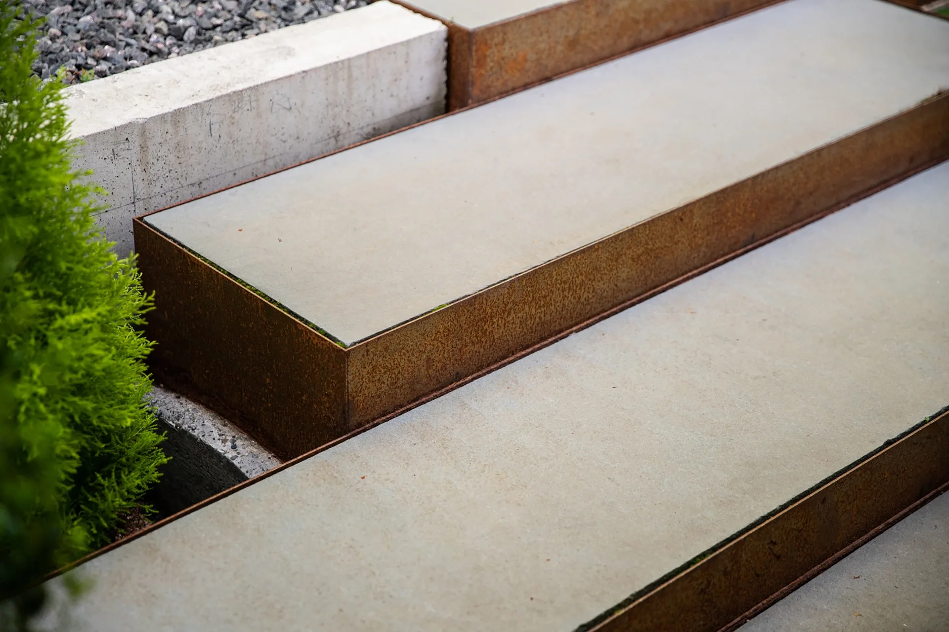 Close-up view of concrete landscape steps bordered by rusted metal frames next to a green shrub.