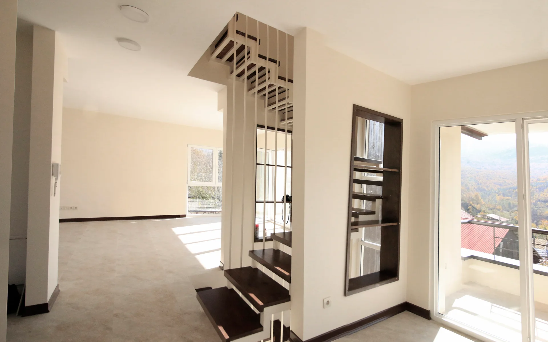 A minimalist open-plan room features an open-riser staircase with dark wood treads, white vertical steel railings, and a built-in dark wood niche.