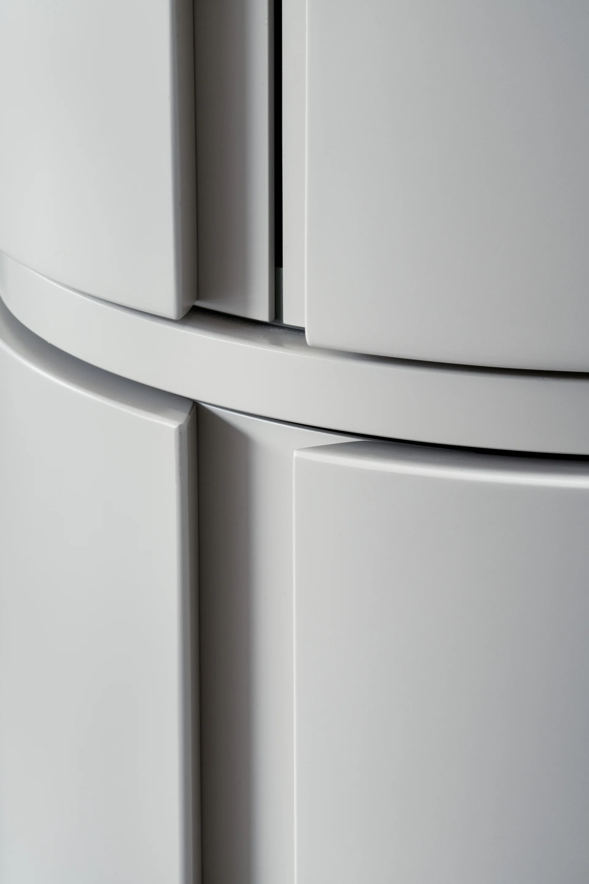 Close-up of curved light grey cabinetry panels showing a smooth satin lacquer finish and minimalist handleless design.