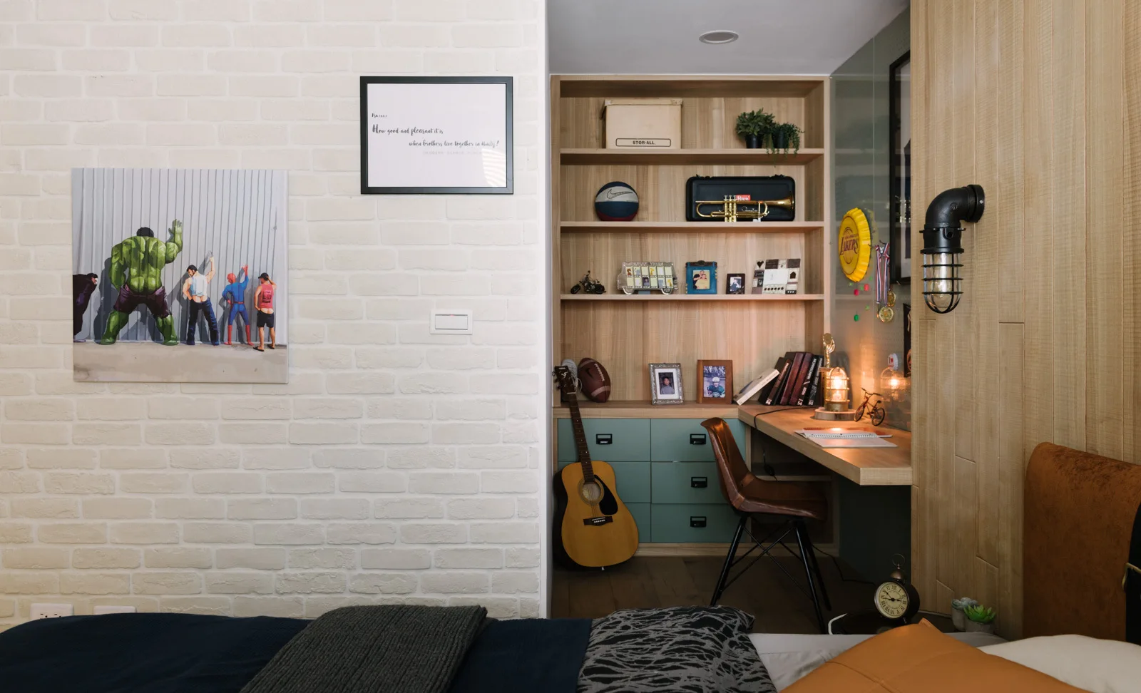 A built-in wooden desk with muted green drawers and shelving is tucked into a bedroom corner next to a white painted brick wall.