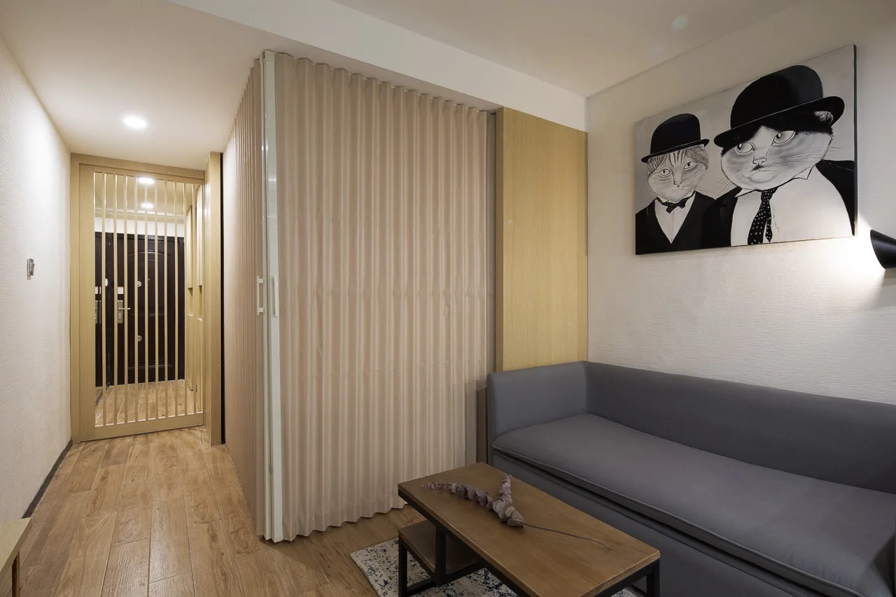A small modern living room features a grey sofa, a wooden coffee table, and a pleated beige accordion partition wall.