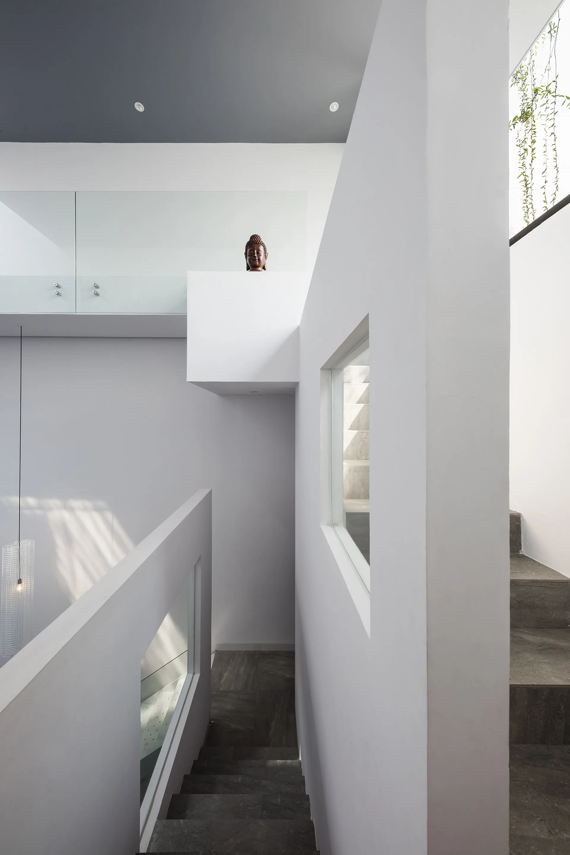A multi-level white stairwell features dark grey stone treads, clean glass railings, and a square window cut-out.