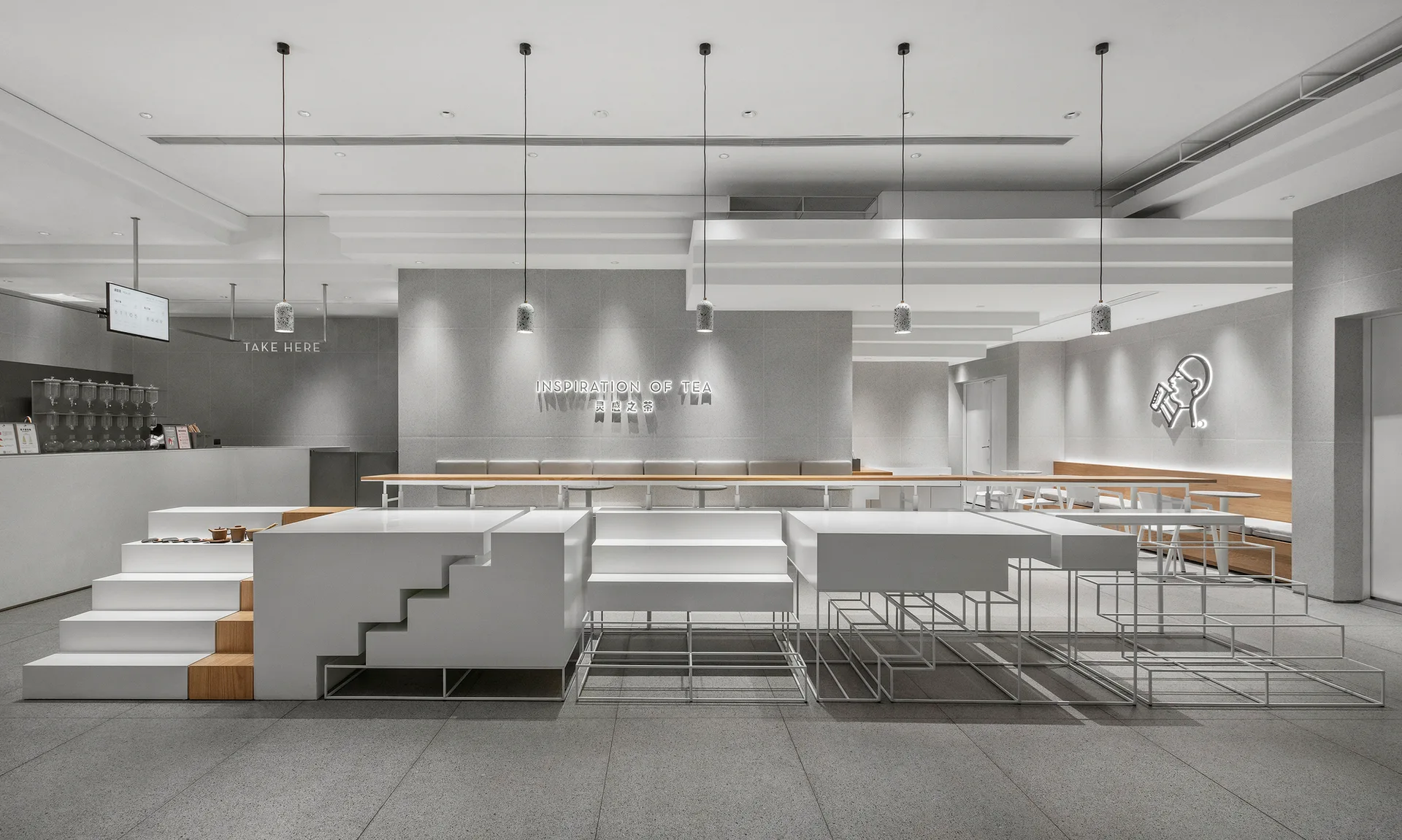 A minimalist commercial cafe interior features a large white tiered seating structure, stone-textured gray walls, and slim pendant lights.