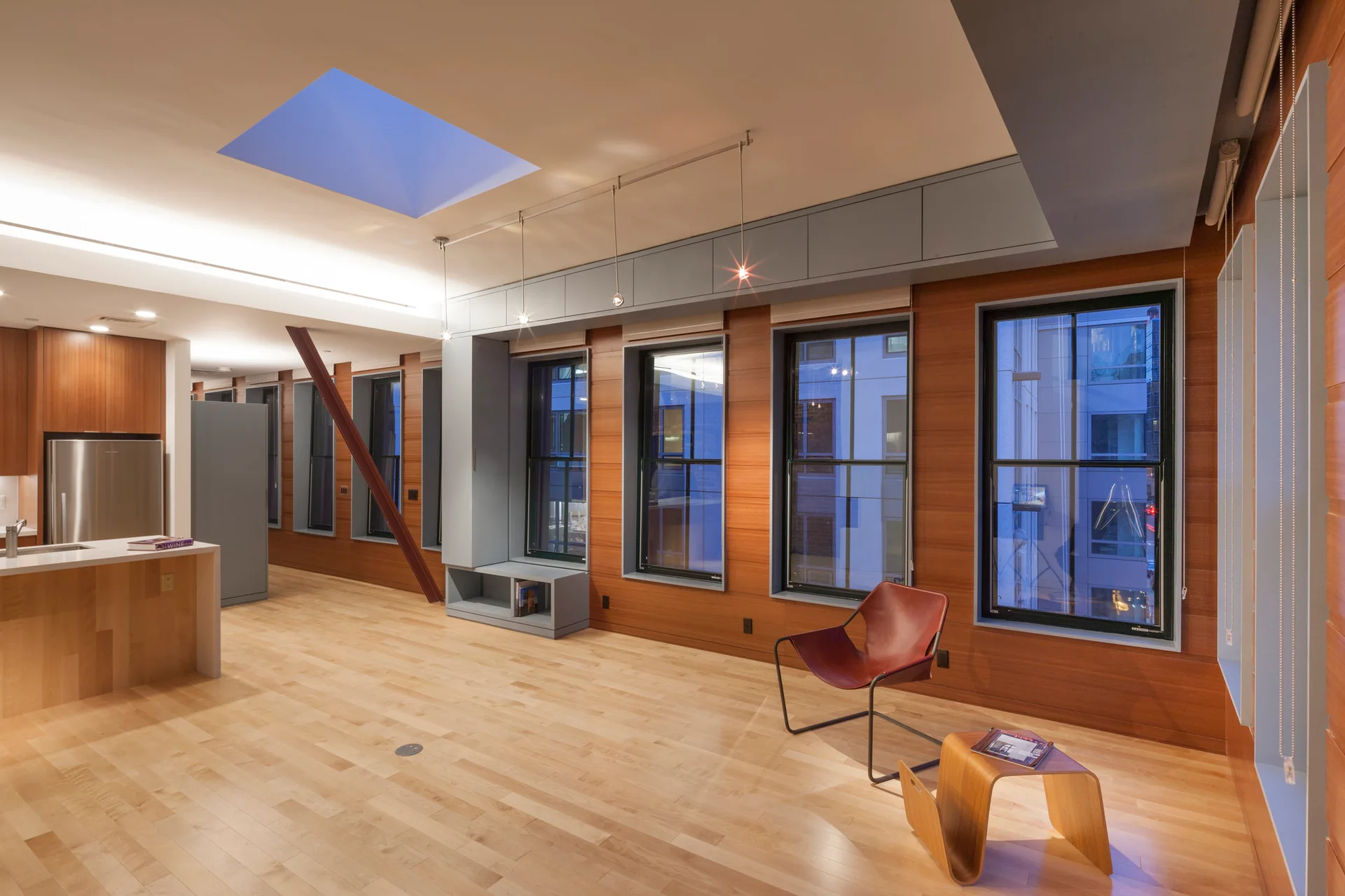 A spacious loft living area featuring warm wood wall paneling, a red accent chair, and a square ceiling skylight.