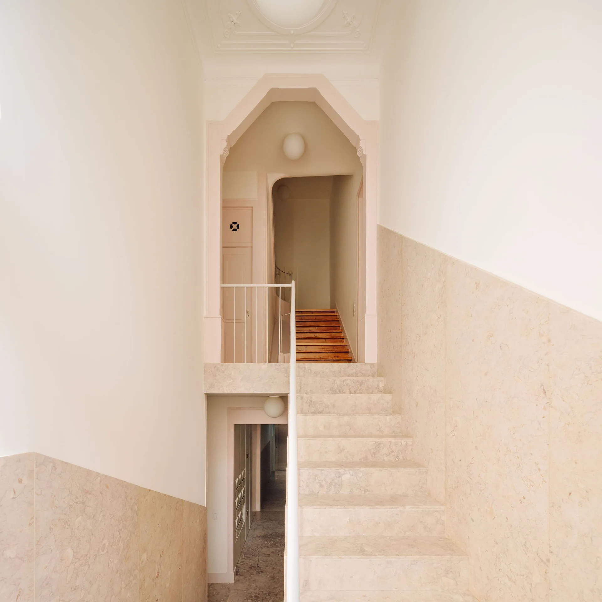 An interior staircase with beige stone steps and diagonal stone wall cladding leads up to a shaped geometric archway.
